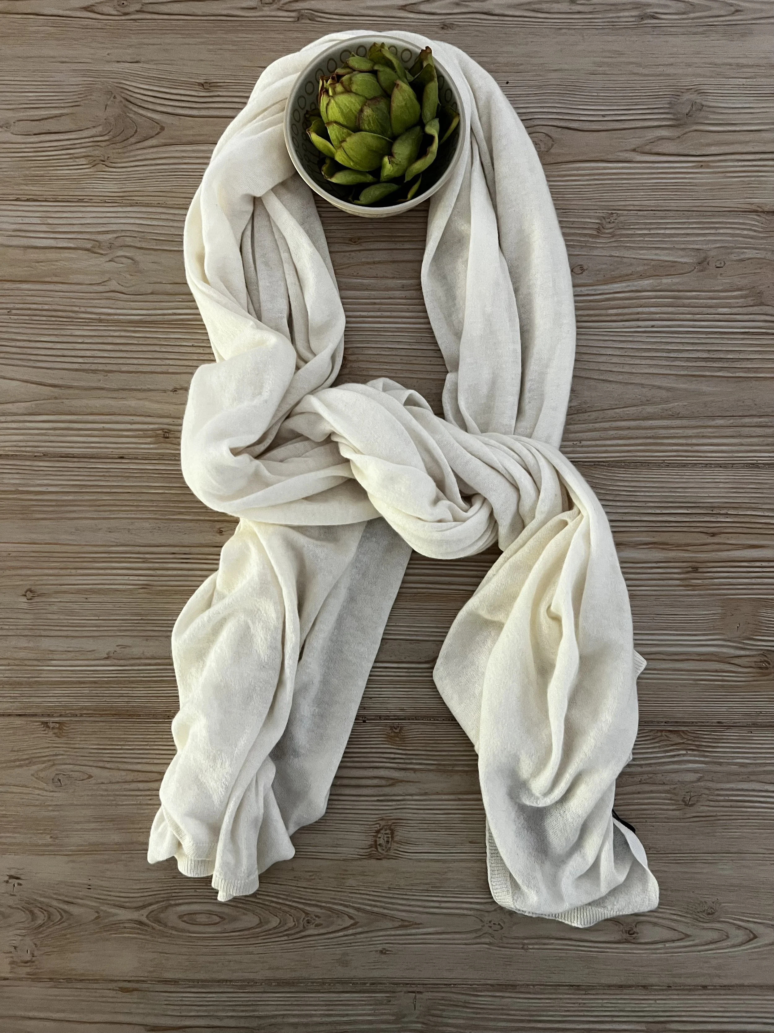 A bowl of green artichokes resting on a white cloth on a wooden surface.