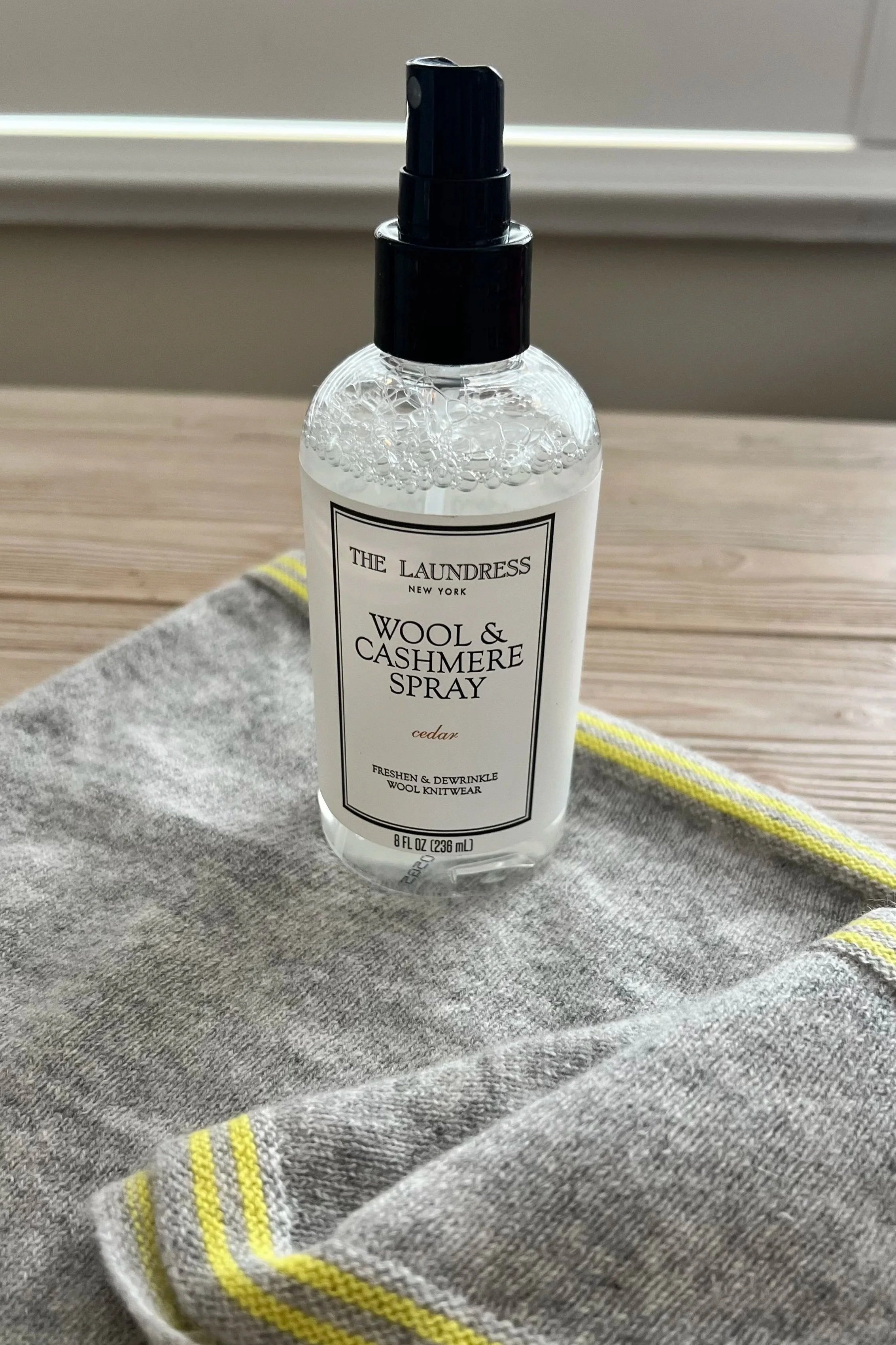 Cashmere refresh spray bottle Wool & Cashmere Spray' resting on a gray cashmere scarf with yellow-striped edges.