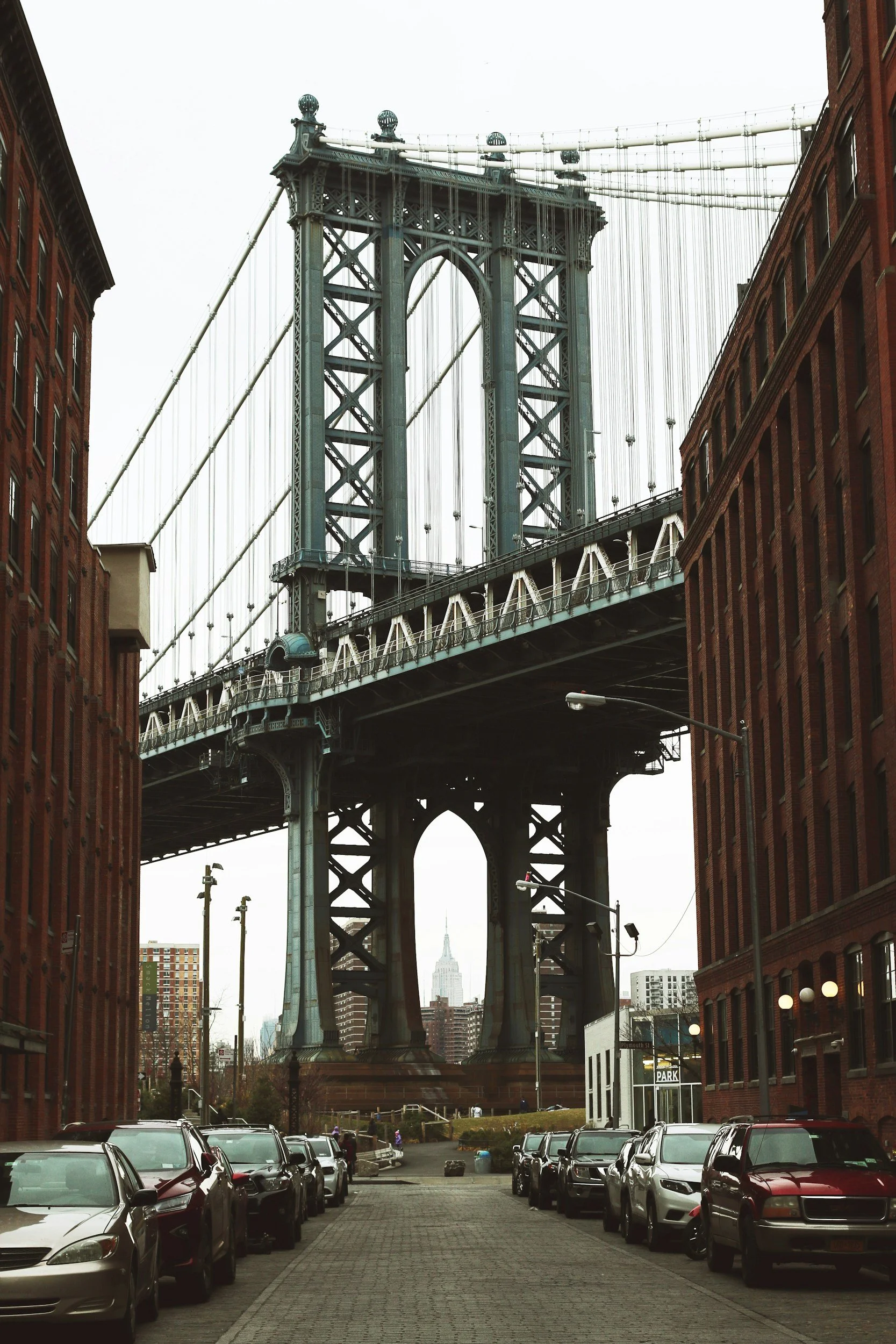 Looking up from a parking lot at the Brooklyn Bridge with the Empire State Building in the background.