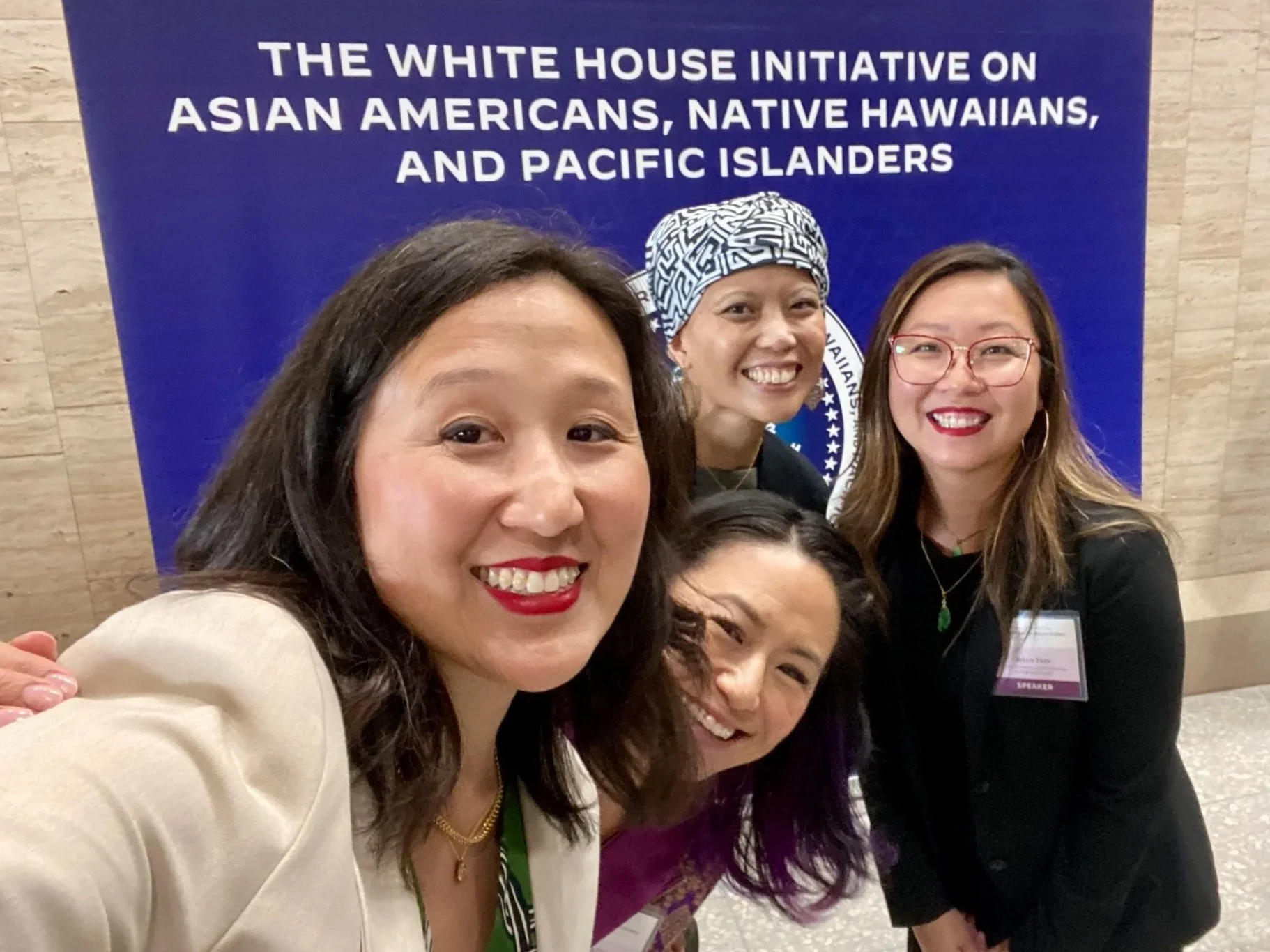 Group of five women smiling and taking a selfie in front of a blue sign that reads 'The White House Initiative on Asian Americans, Native Hawaiians, and Pacific Islanders.'