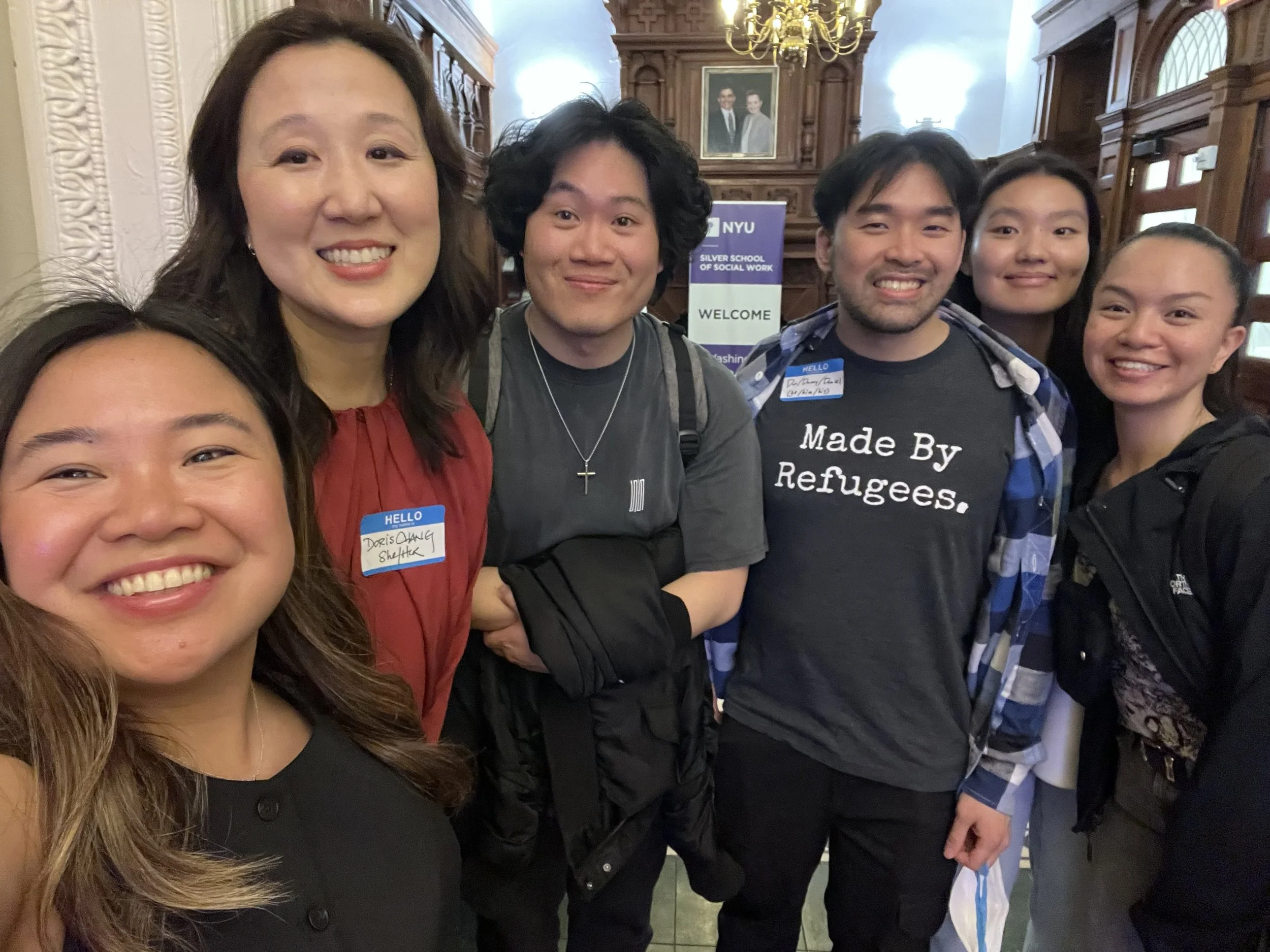 Group of six smiling people standing inside a building with wood-paneled walls and a chandelier, during an event at NYU Silver School of Social Work.
