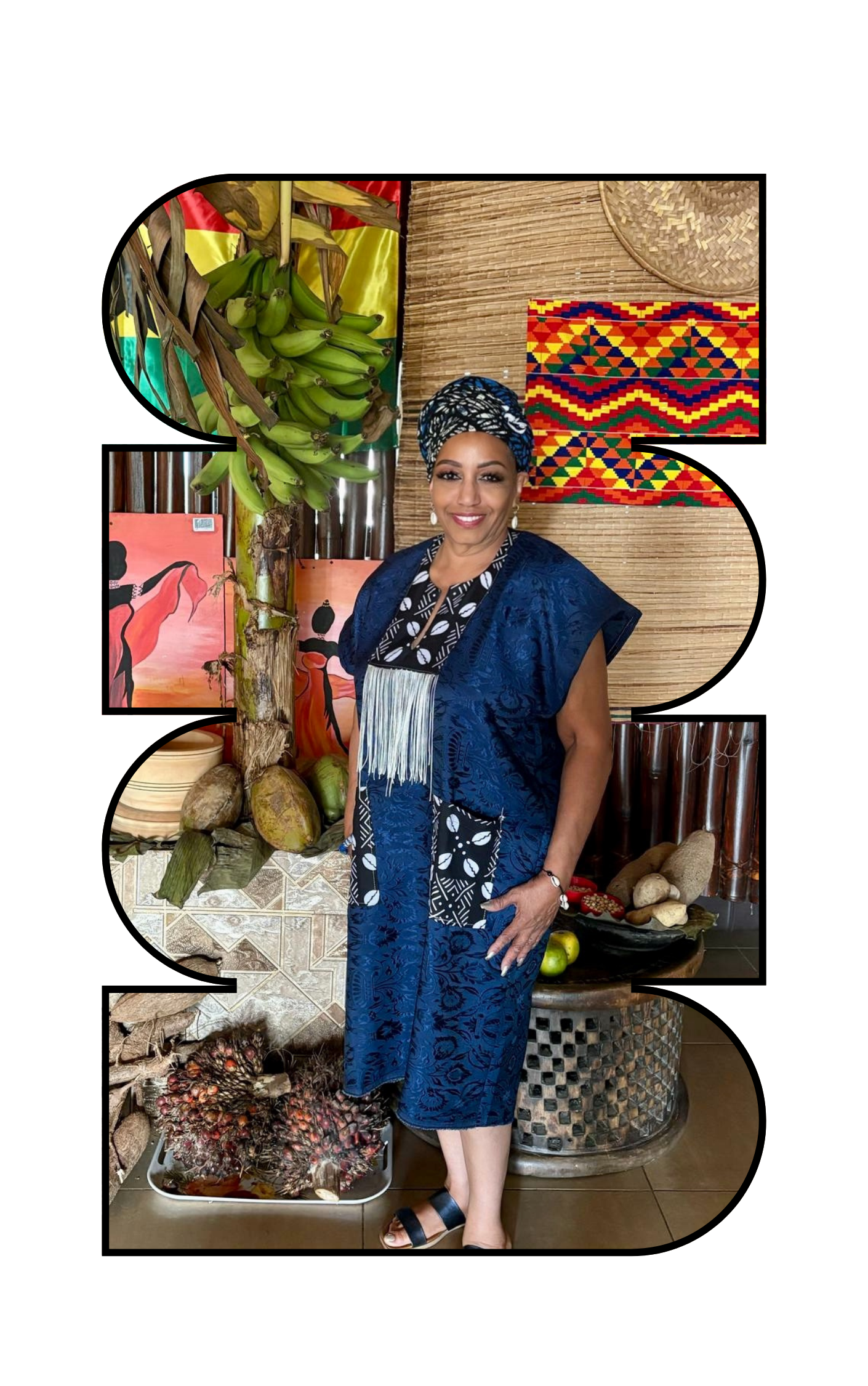 Woman in traditional African attire standing indoors surrounded by cultural decorations, including banana leaves, fruits, and artwork with vibrant patterns.