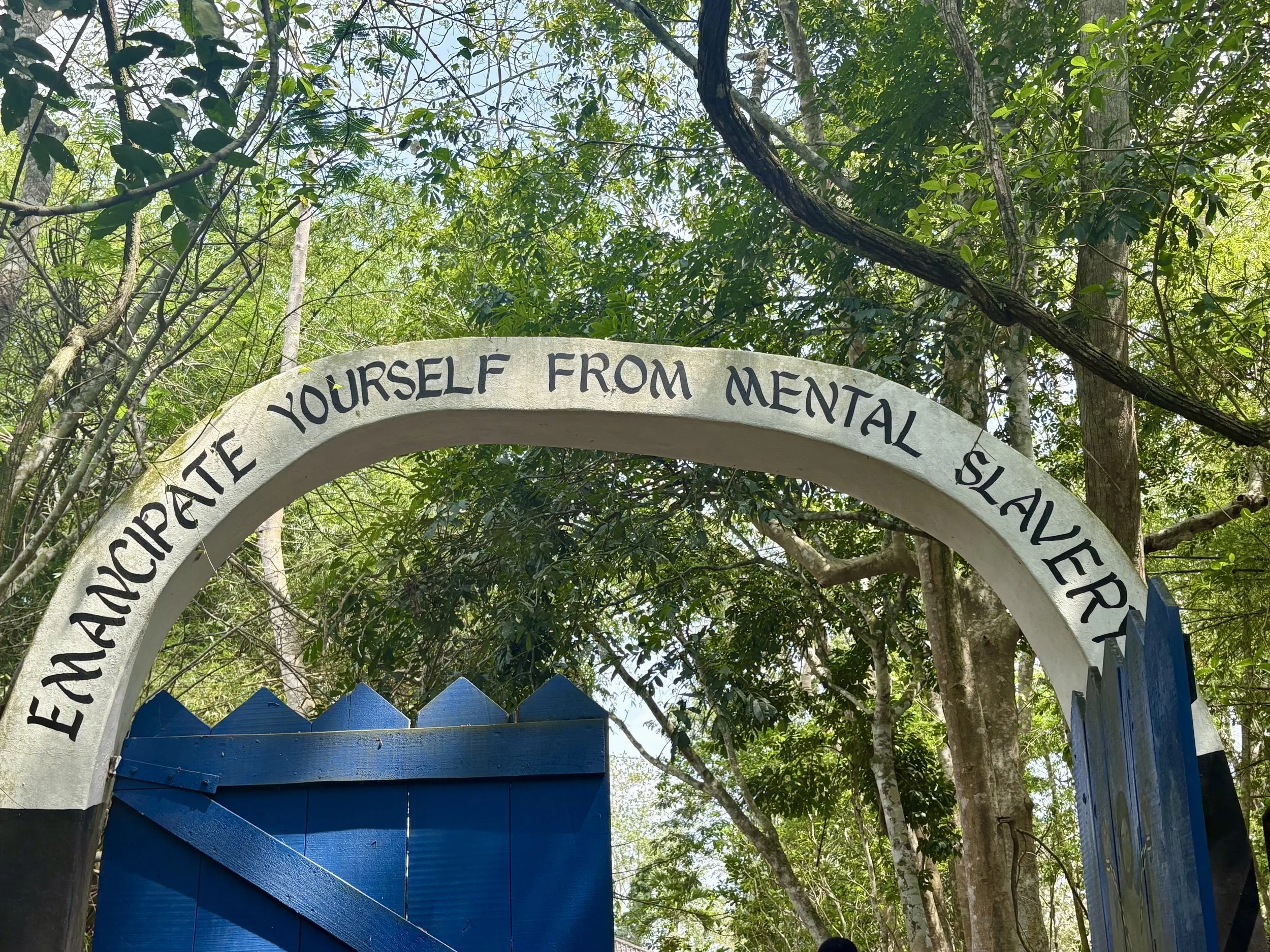The entrance archway to a forested area with the quote 'Emancipate yourself from mental slavery' written on it.