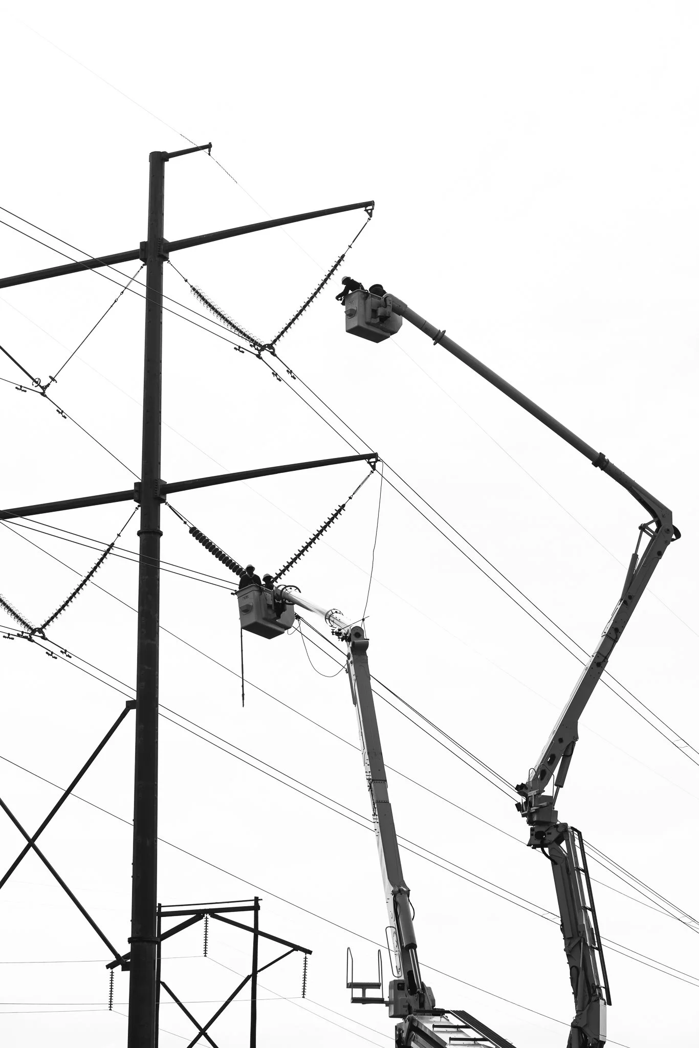 Two workers operating lift buckets on trucks repairing electrical power lines.