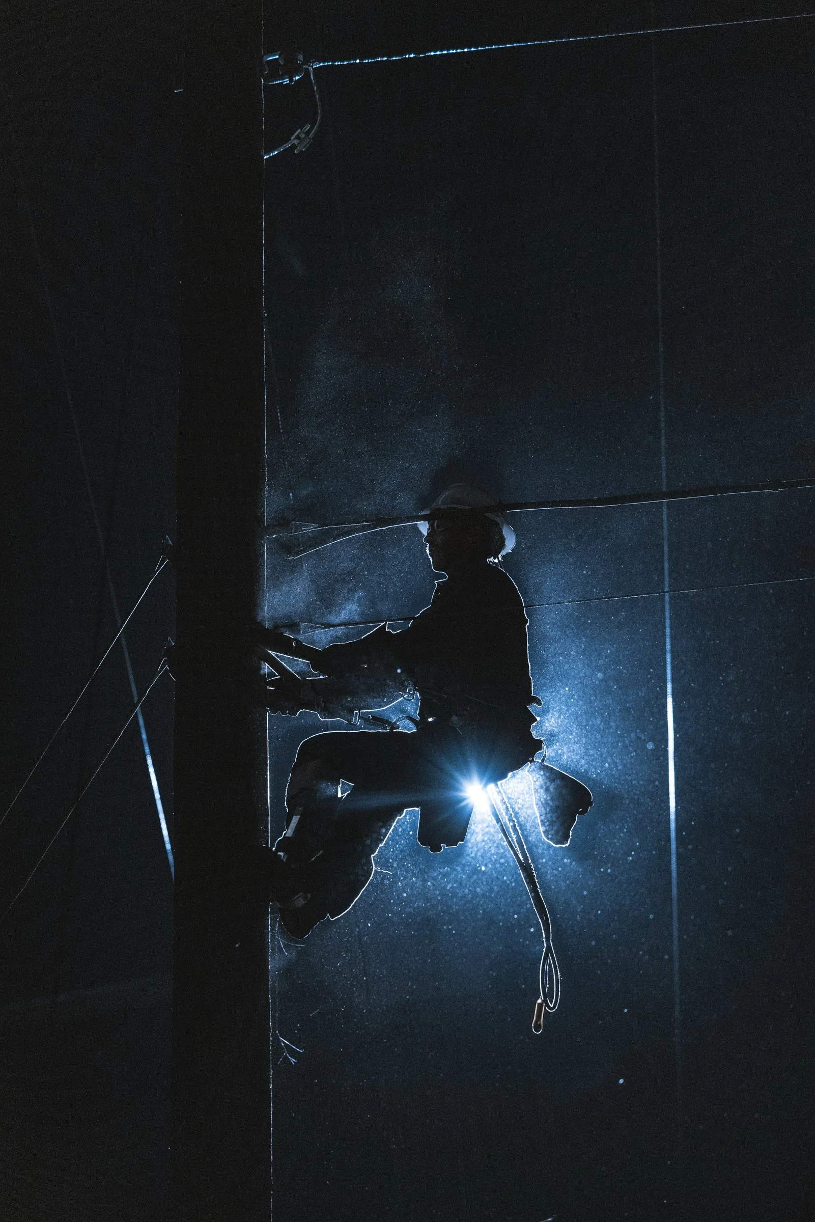 Silhouette of a worker climbing a utility pole at night with a bright light behind them