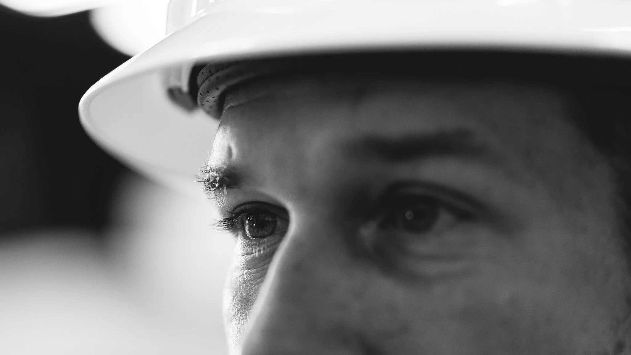 Close-up black and white photo of a person's face, focusing on the eyes, with a hood or hat partially covering the head.
