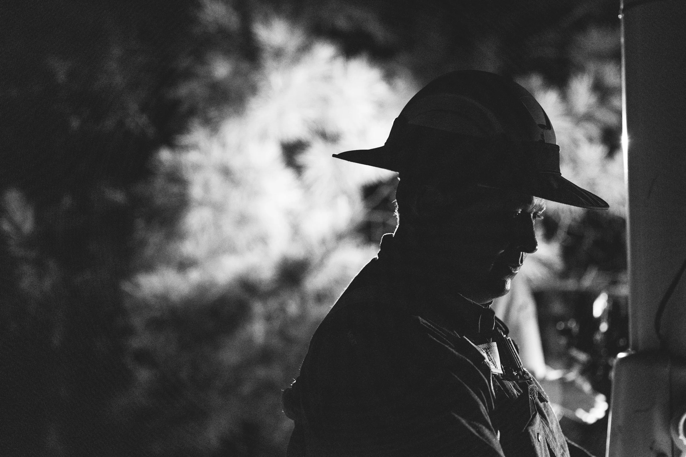 A silhouette of a man wearing a cap and a uniform, working with a piece of equipment, in a dimly lit environment with blurred background.