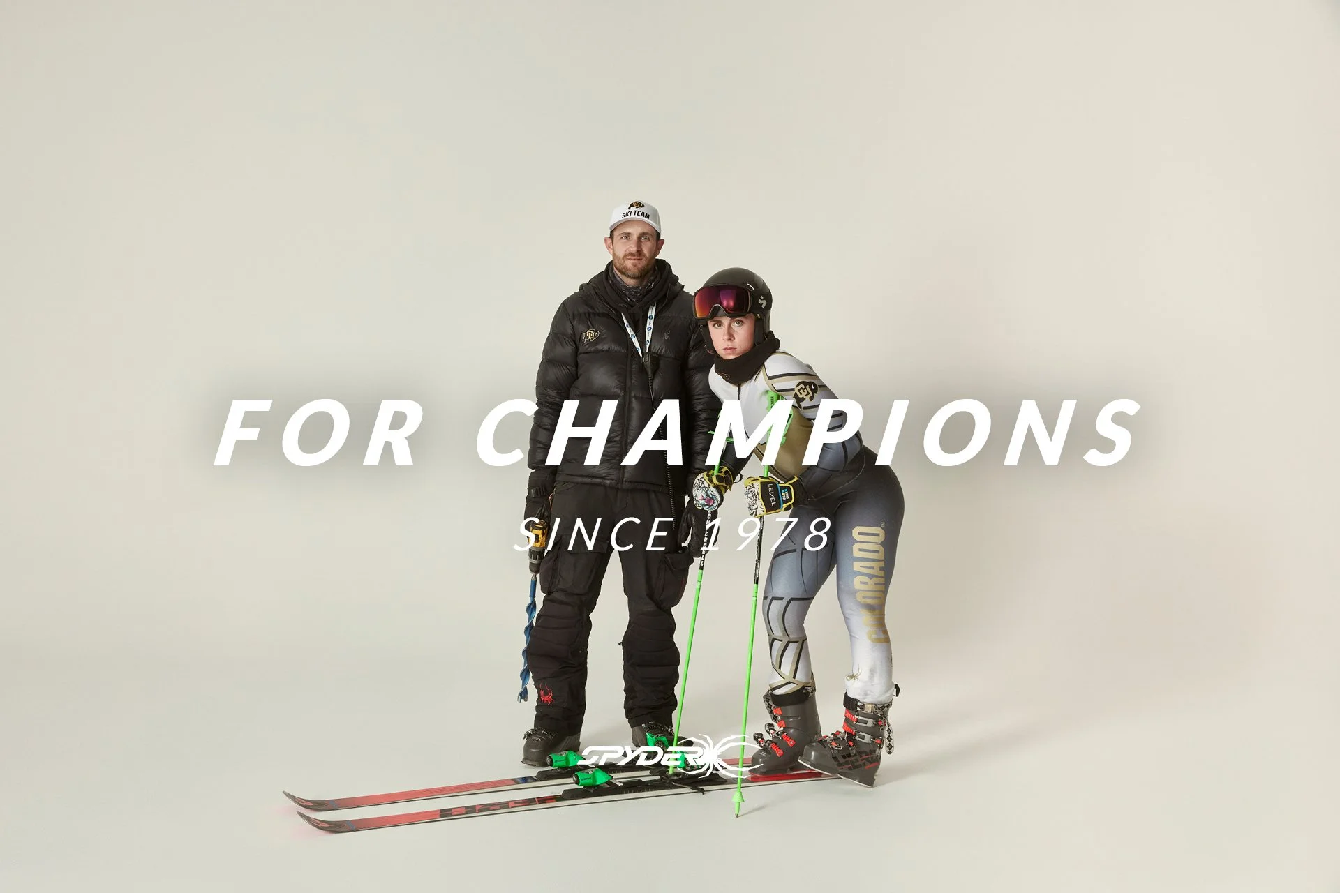 A male ski coach standing next to an female skier in racing gear, both on skis, with the text 'For Champions Since 1978' written across the image.