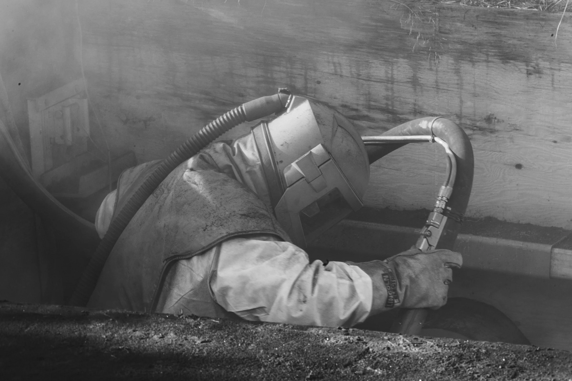 A construction worker wearing protective gear and gloves, operating a tool inside a trench or small excavation.