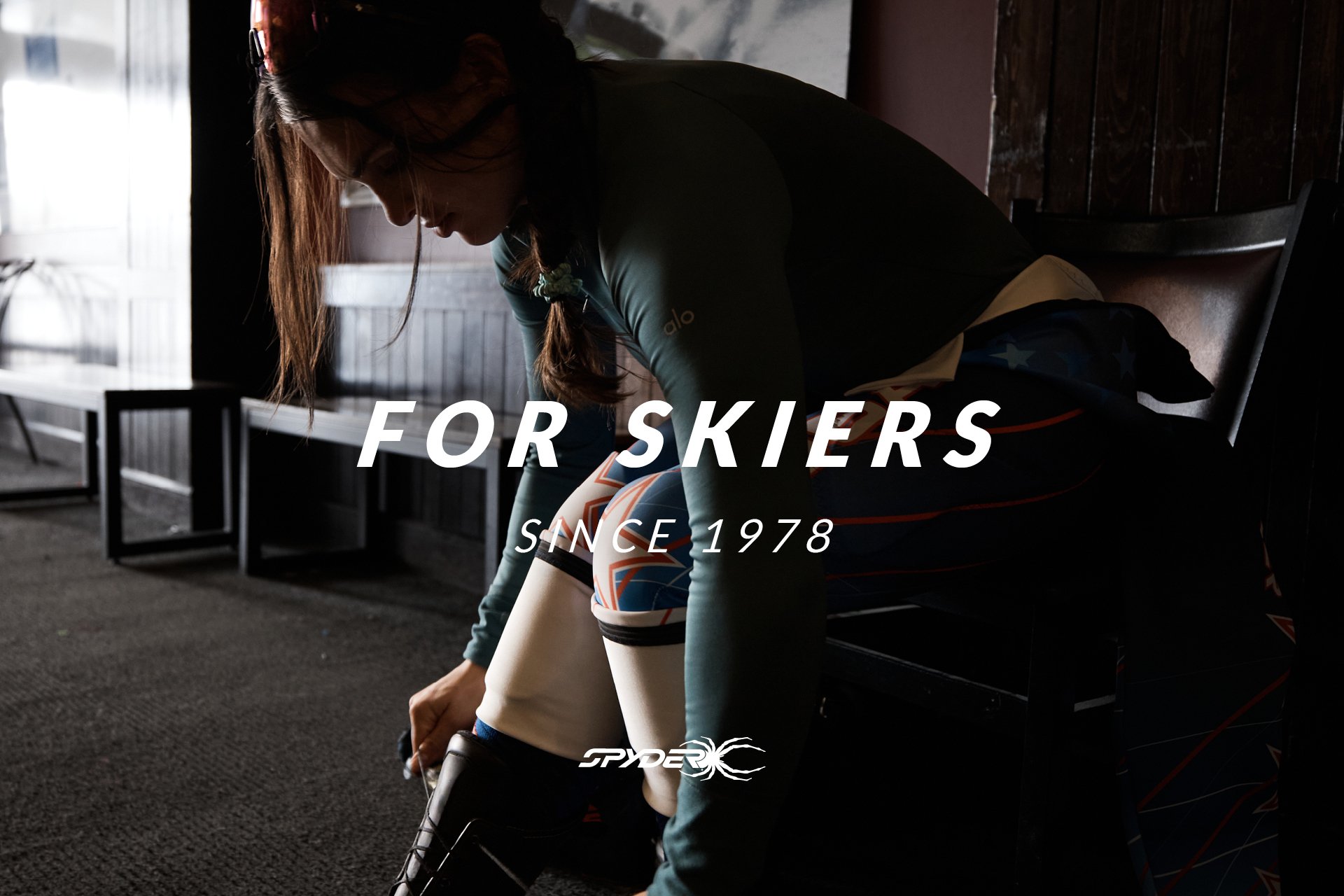 A woman in ski gear putting on a ski boot inside a ski lodge, with a bench and a window in the background. Overlay text reads 'For Skiers Since 1978' and the Spyder logo.
