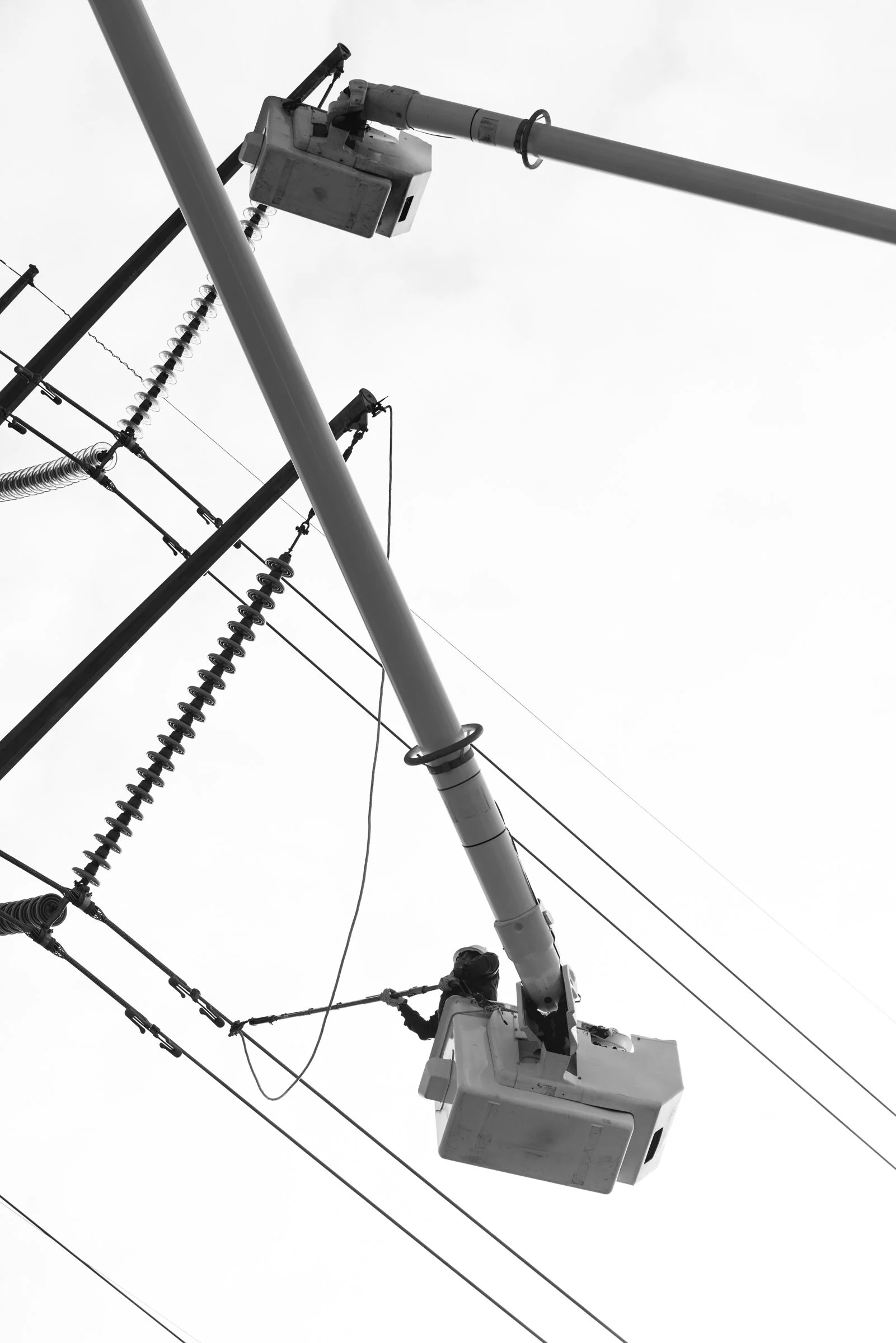A worker on an aerial lift working on electrical power lines against a cloudy sky.