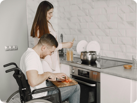 An elderly man comforting an elderly woman with short white hair and glasses in a kitchen.
