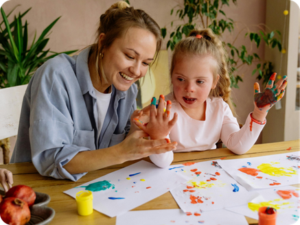 Woman and young girl painting with colorful paints at a table, smiling and enjoying their activity.
