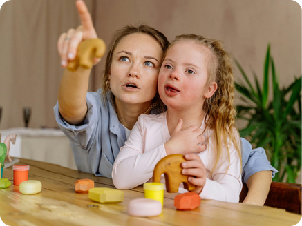 A woman and a young girl, possibly mother and daughter, playing with wooden toys at a table. The woman is pointing at something off-camera with a concerned expression, while the girl holds a wooden toy and looks in the same direction.