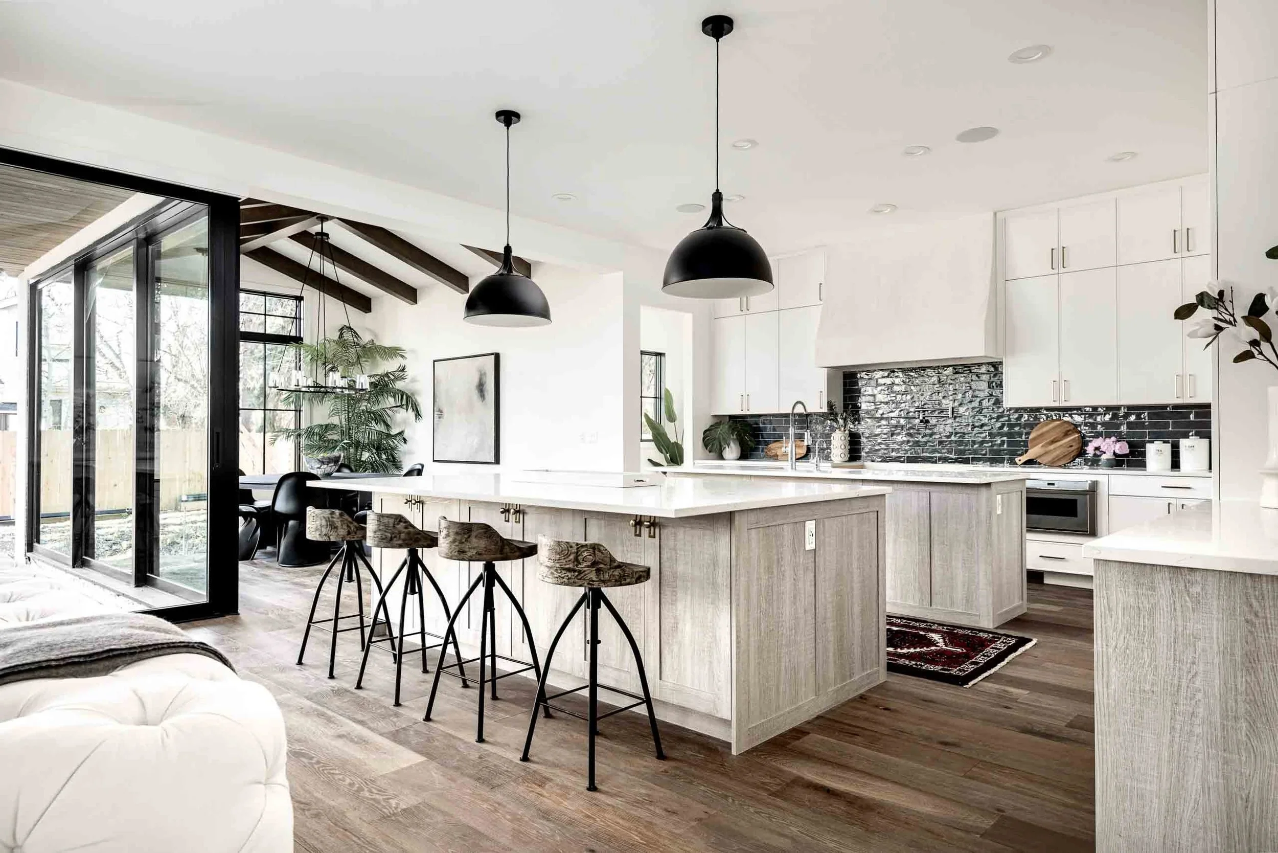 Modern kitchen with white cabinetry, black backsplash, island with barstools, and black pendant lights.