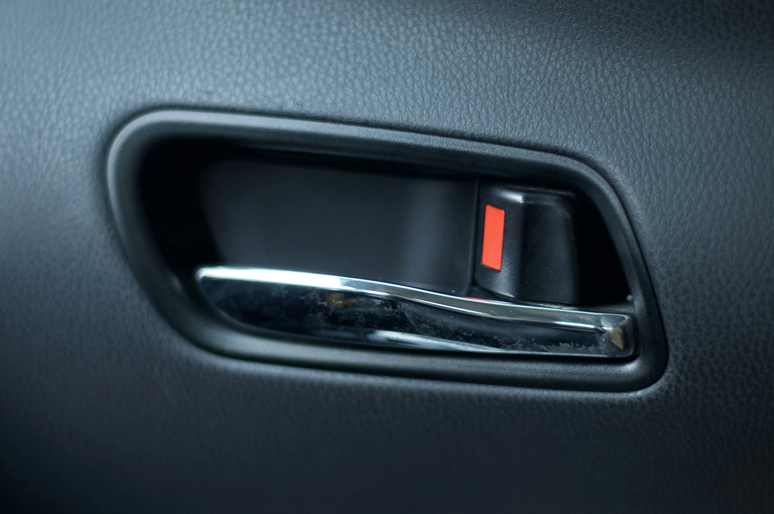Inside view of a car door handle with a red latch.
