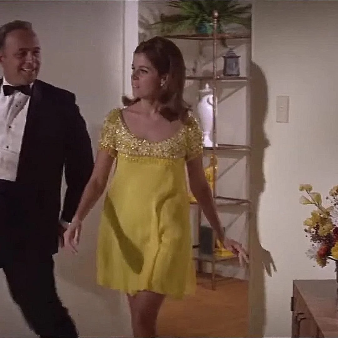 A man in a tuxedo and a woman in a yellow dress holding hands and smiling.