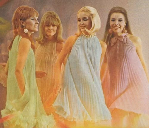 Four women dressed in colorful, vintage dresses standing together and smiling.