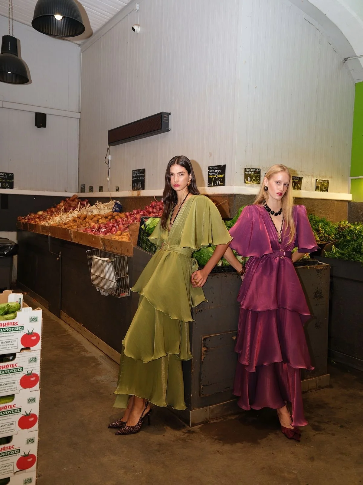 Two women in colorful, flowing dresses inside a grocery store by fresh produce section