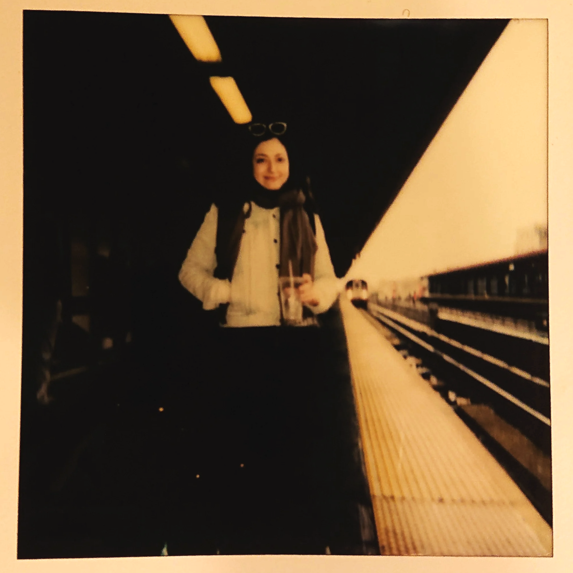 A photograph of Charline Tetiyevsky wearing sunglasses, standing on a subway platform, holding a drink.