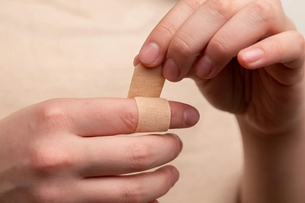 Person applying a beige adhesive bandage to their finger.
