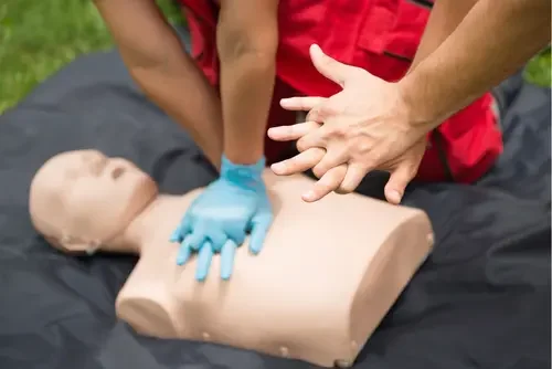 Person practicing hands-only CPR on a training mannequin outdoors
