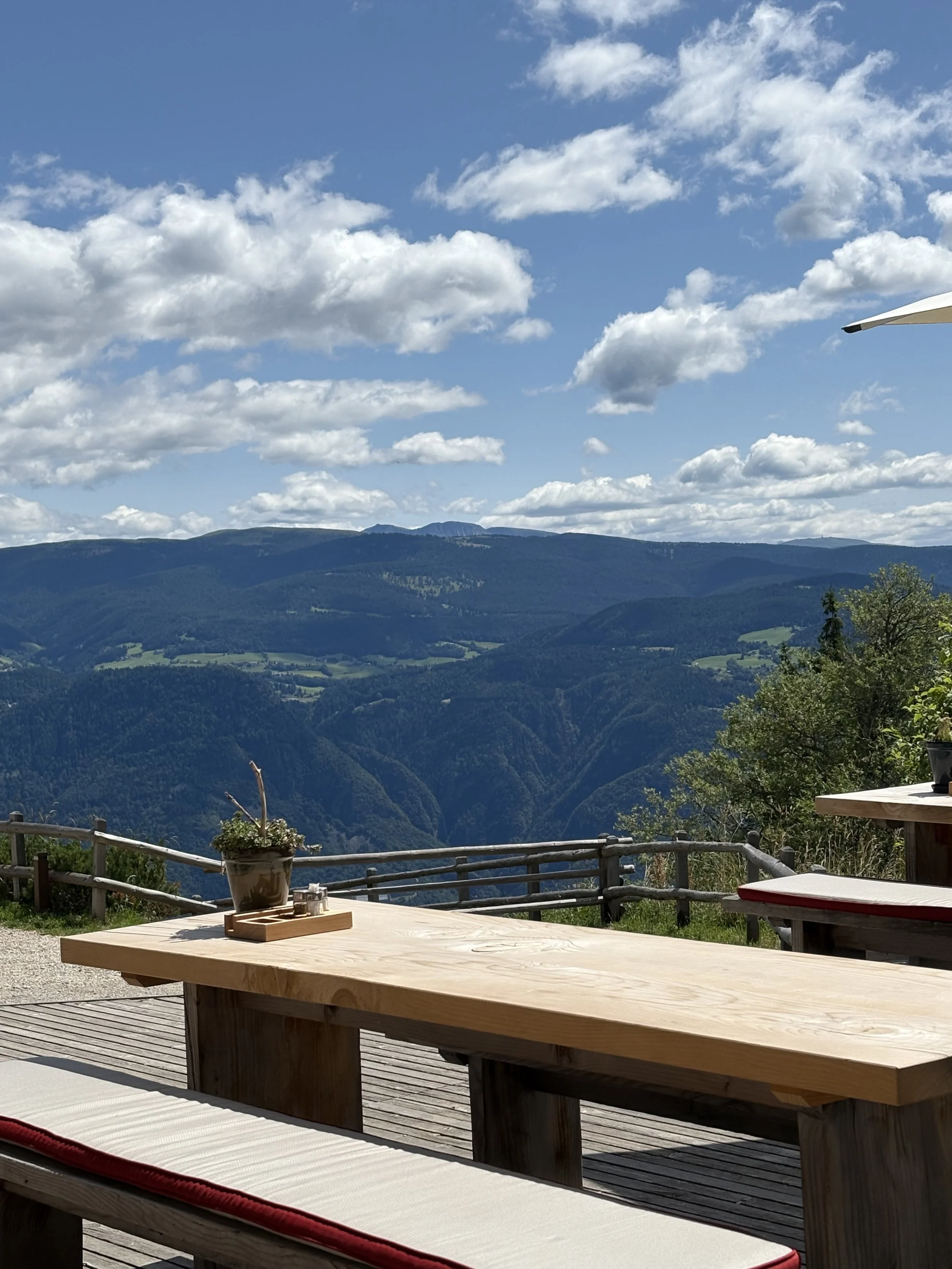 Outdoor seating area on a wooden deck with a view of mountains and a partly cloudy sky.