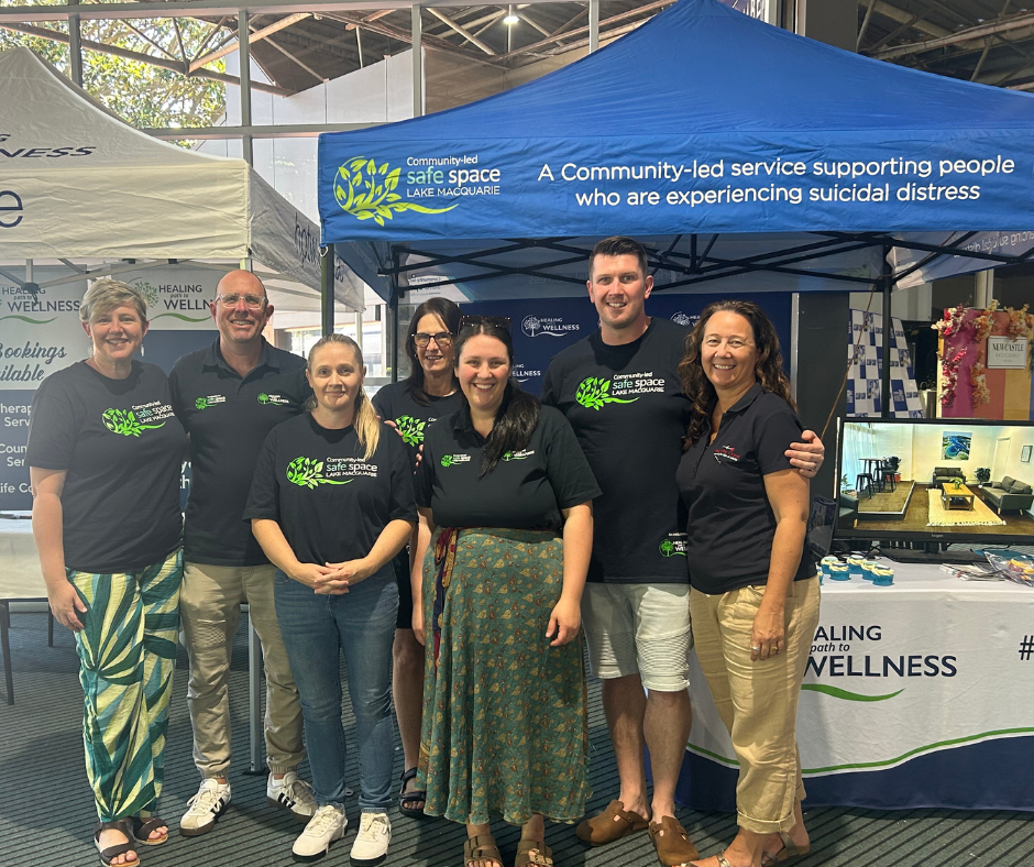 Group of people standing under community-led Safe Space Lake Macquarie booth promoting mental health support for those experiencing suicidal distress.