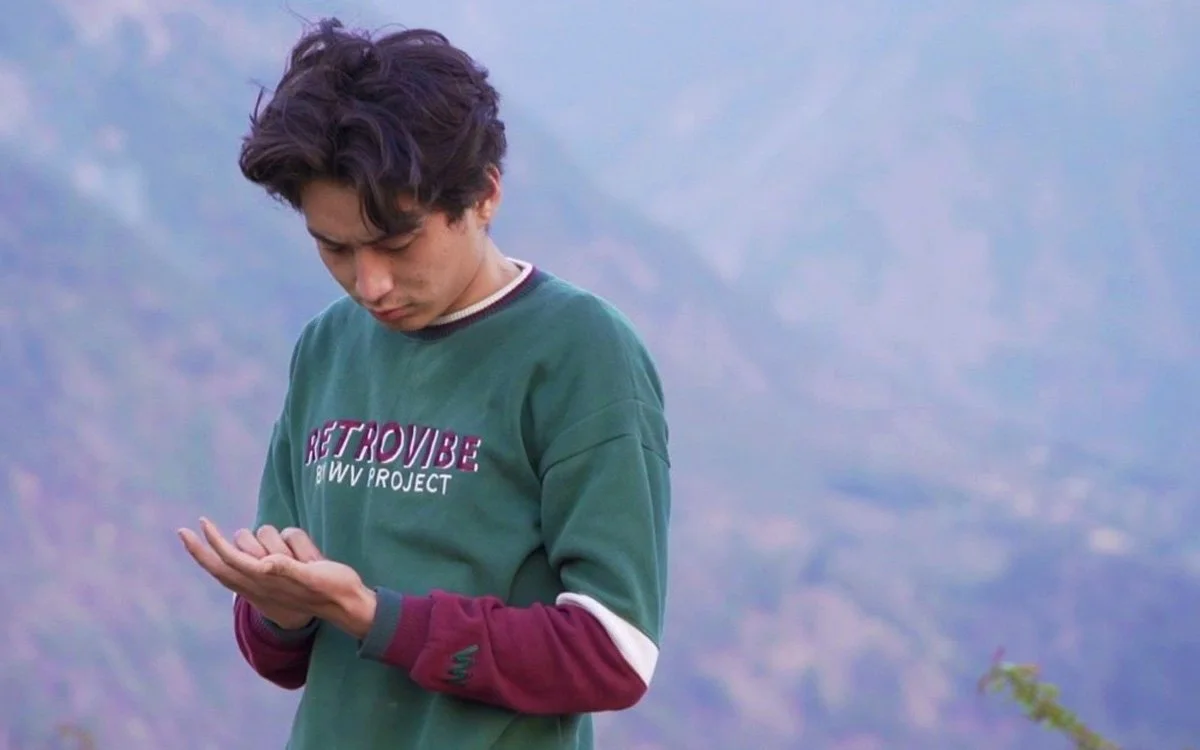 A young man looking at his phone outdoors with mountains in the background.