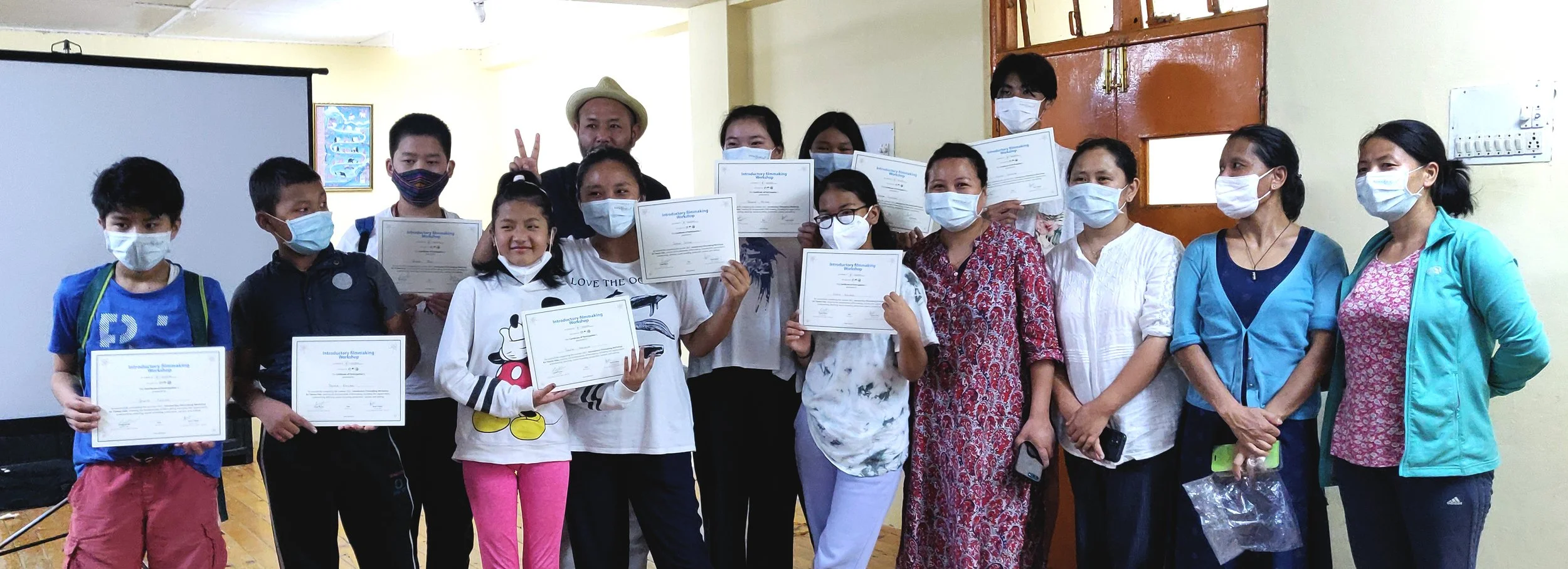 Group of kids and adults holding certificates at a classroom event, all wearing face masks.