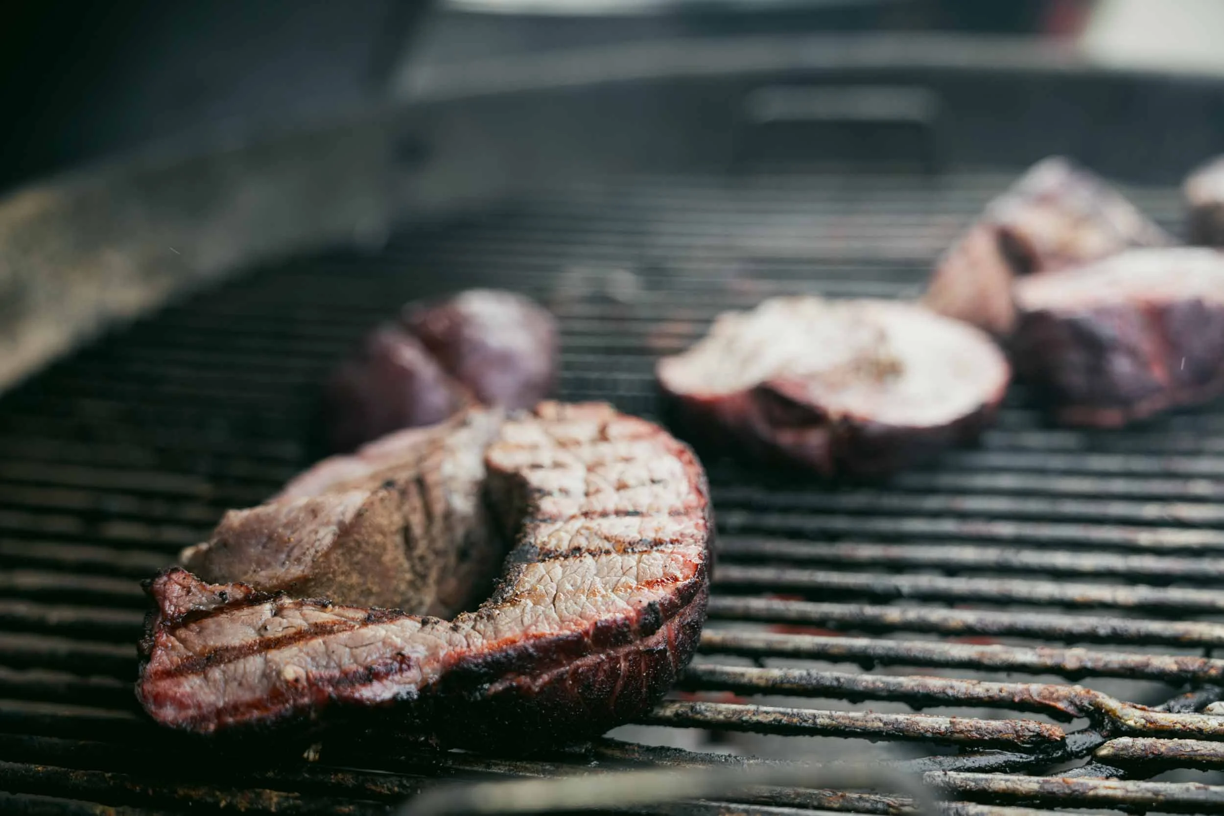Close-up of a grill with two cooked steaks and some mushrooms being grilled.