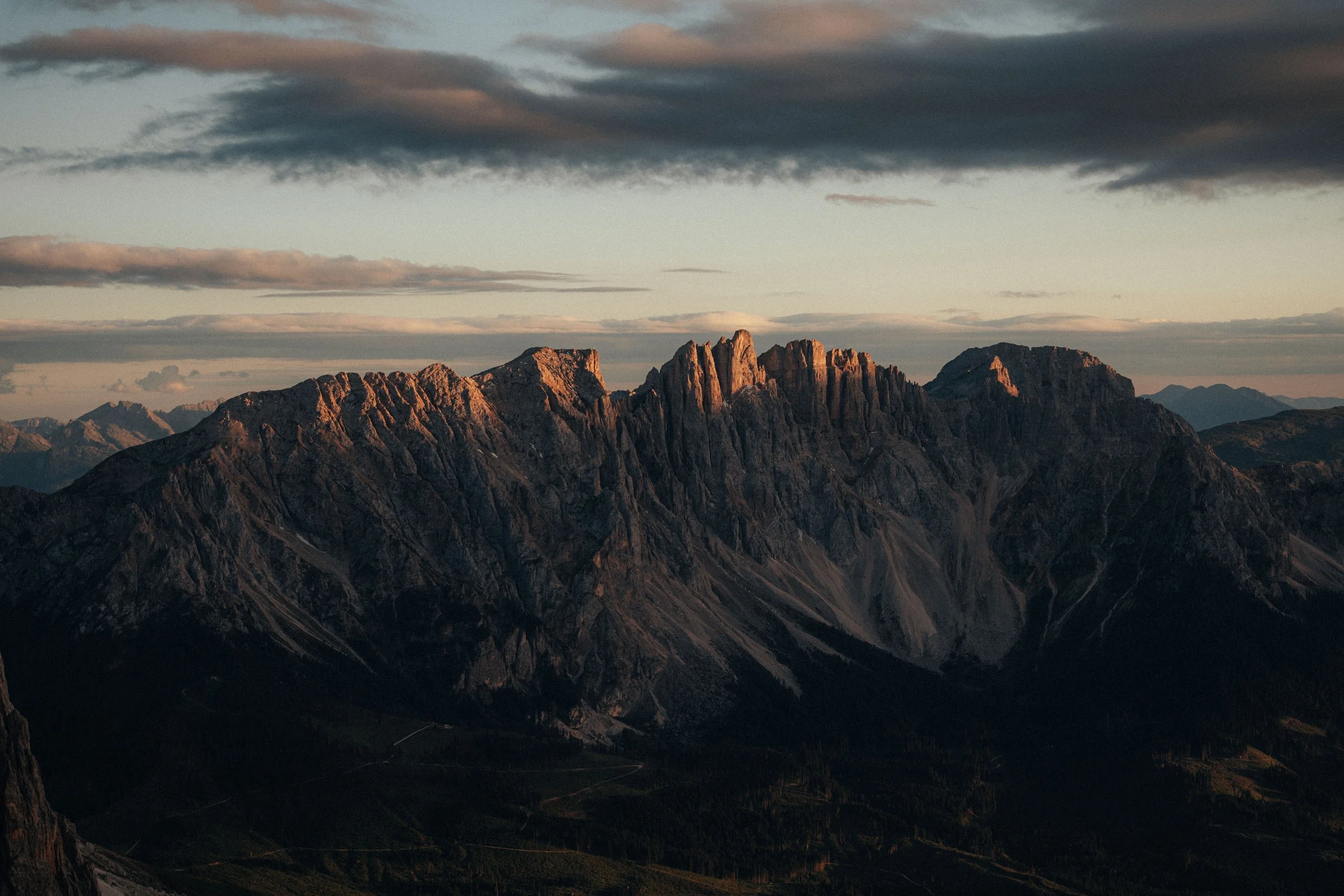 Mountain range during sunset with rugged peaks and a cloudy sky.