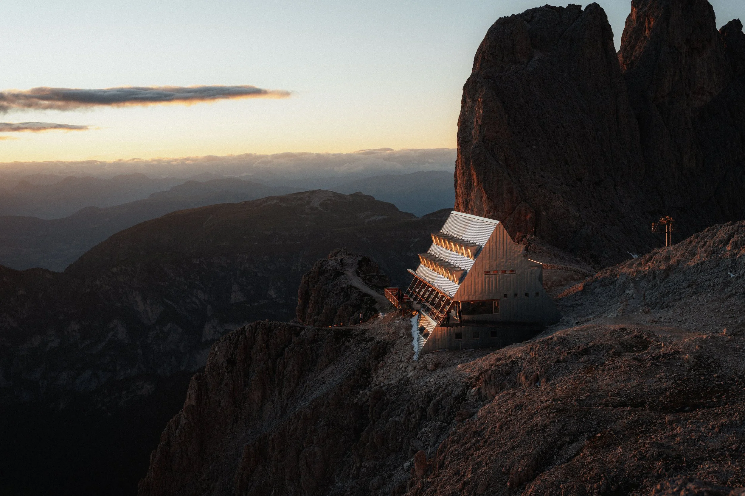 A mountain landscape during sunset with a modern building and large rocks in the foreground.
