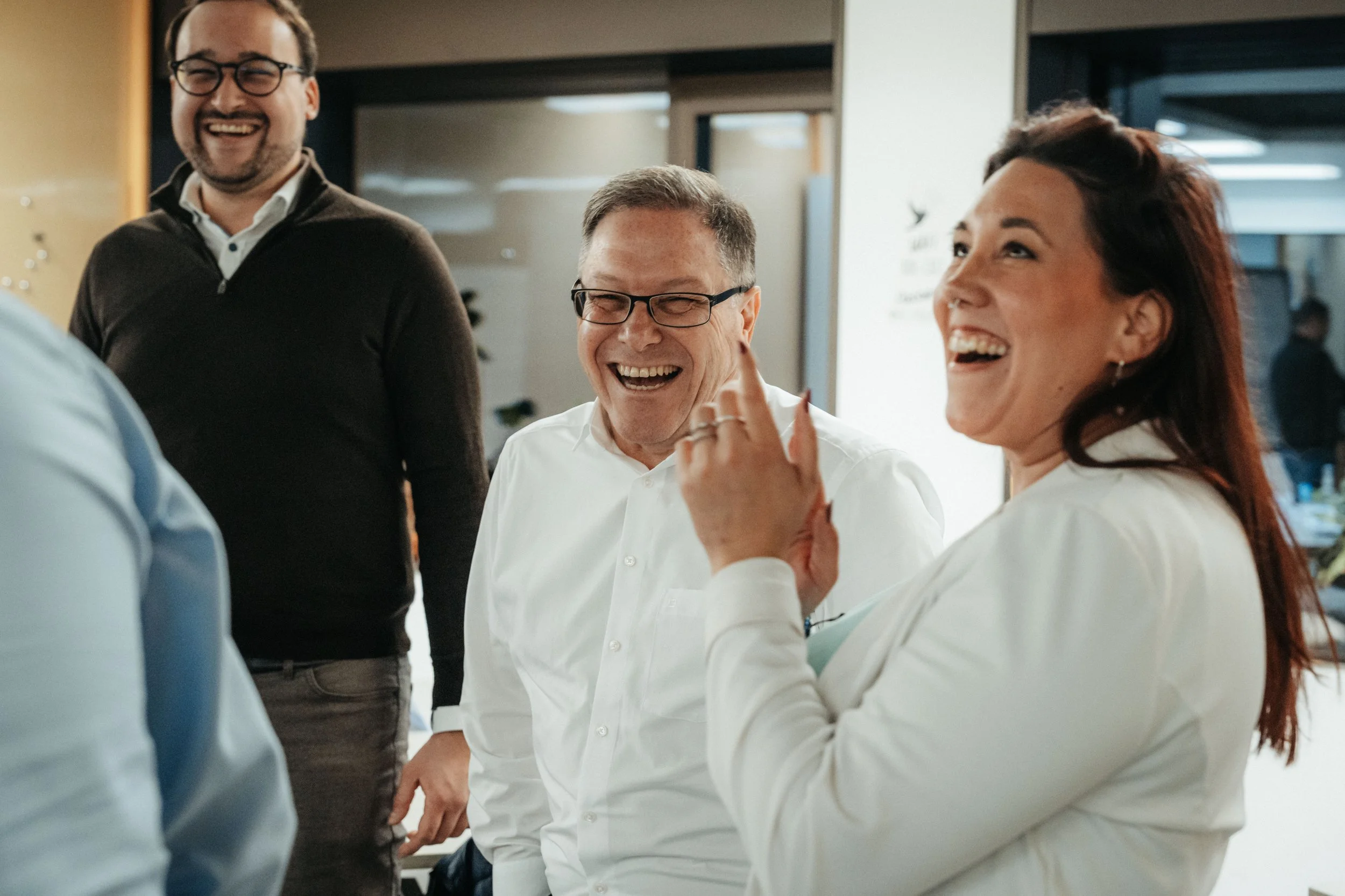 Group of four people laughing and smiling during a conversation in an office setting.