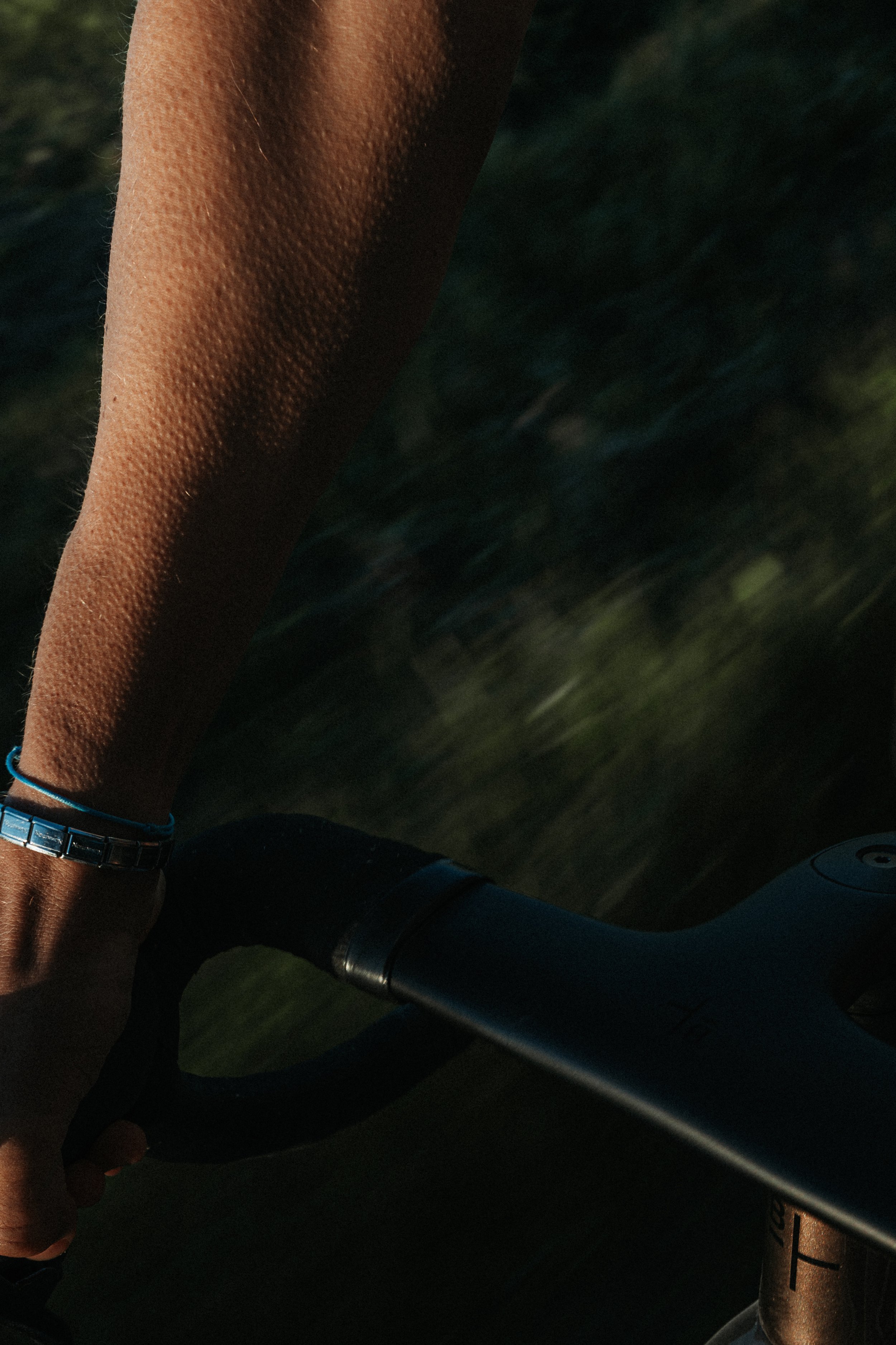 Close-up of a person's arm and hand gripping a bicycle handlebar while riding outdoors at sunset.