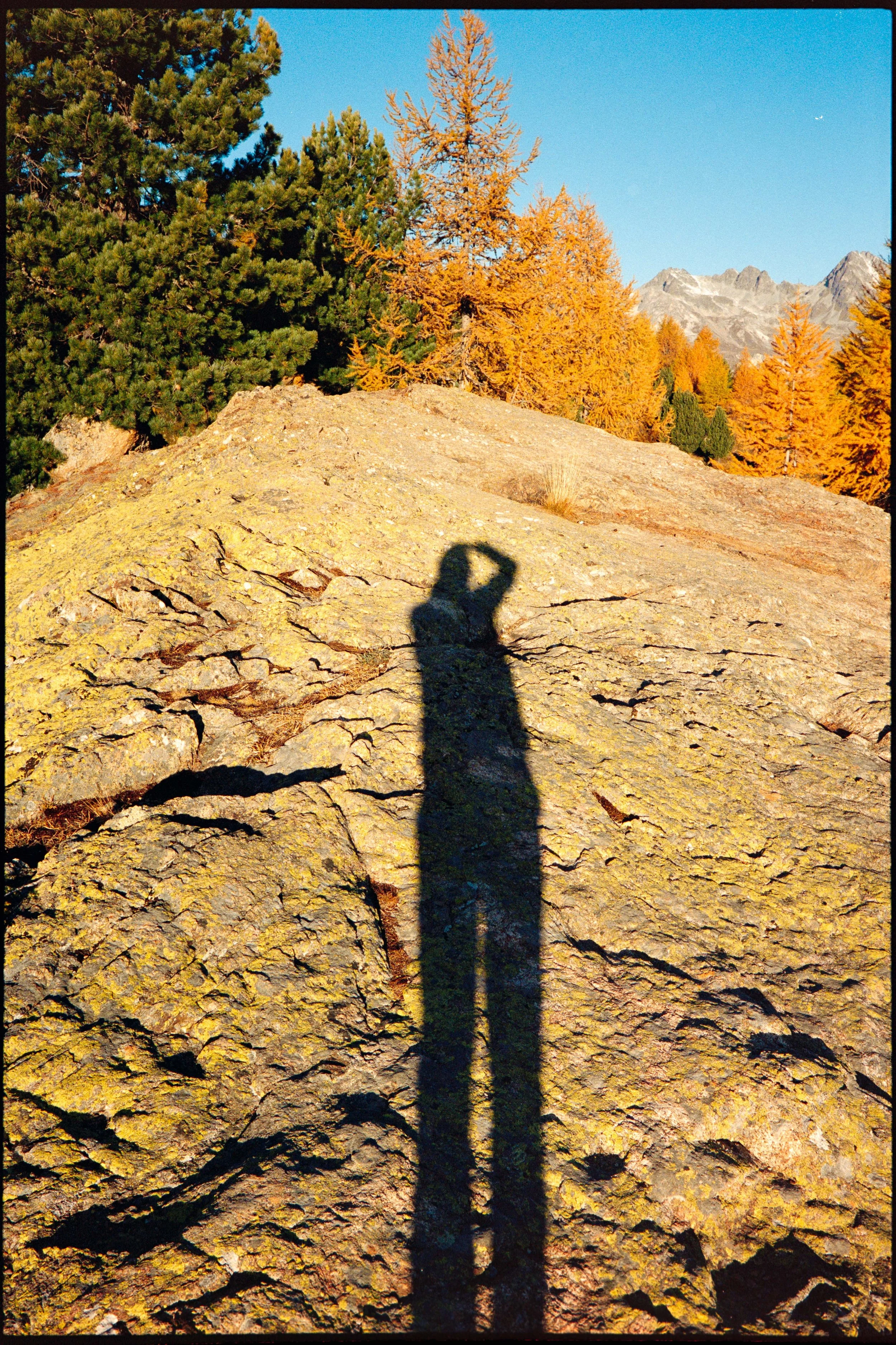 Shadow of a person taking a photo cast on a large rocky surface with trees and mountains in the background.
