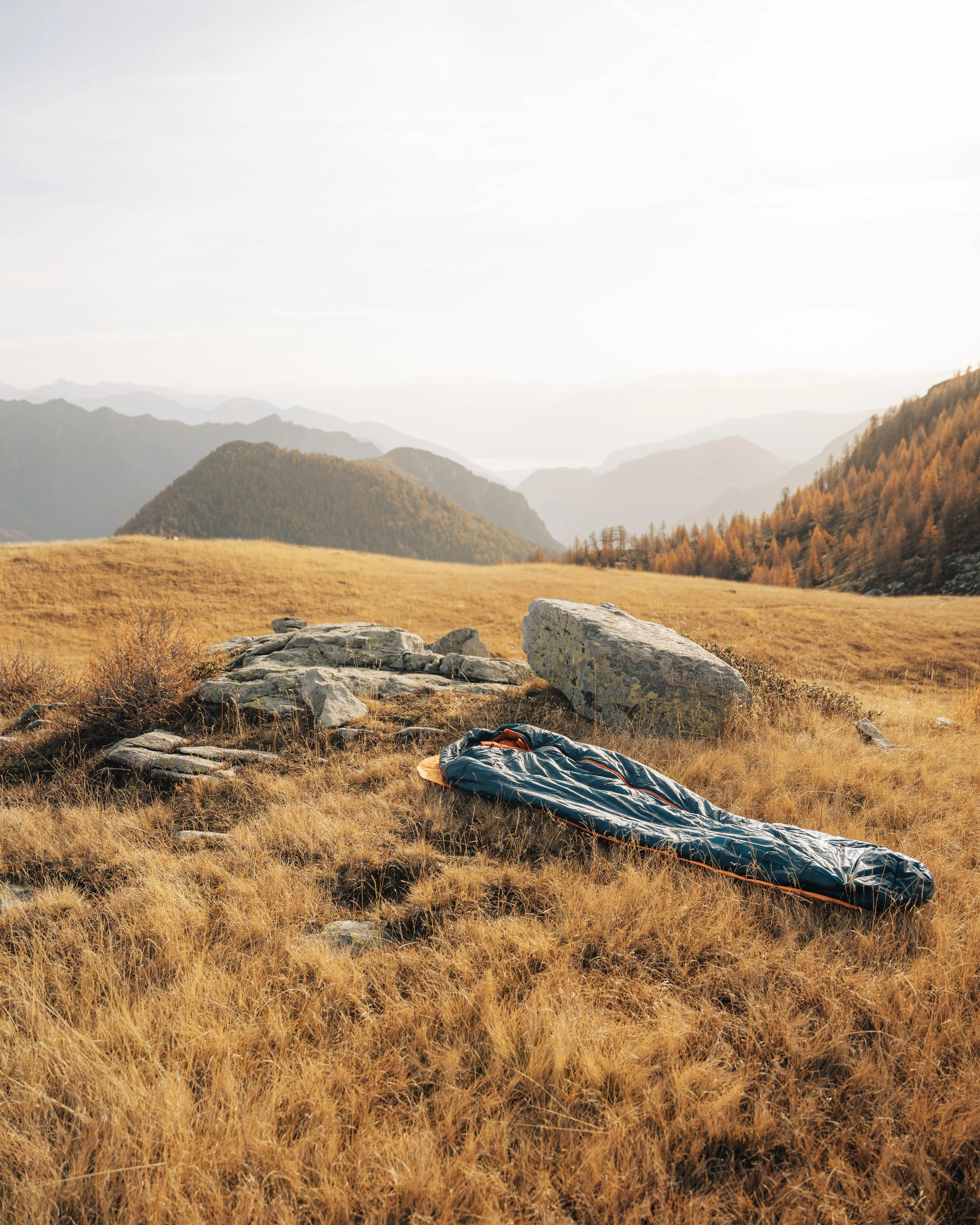 A tent set up on a grassy field in a mountainous area with rocks and trees in the background, under a cloudy sky.