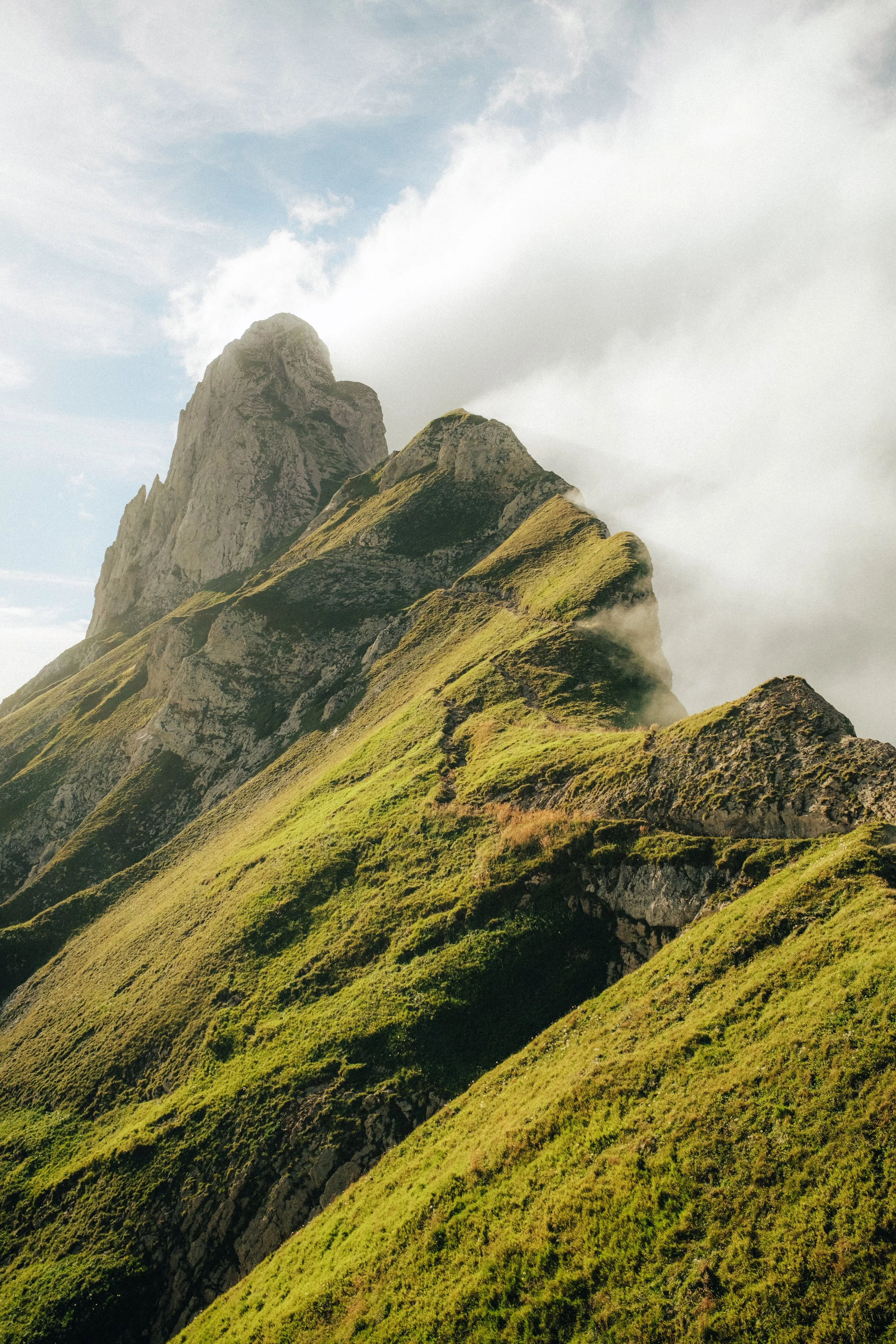 Green, moss-covered mountain with a steep peak in a cloudy sky.