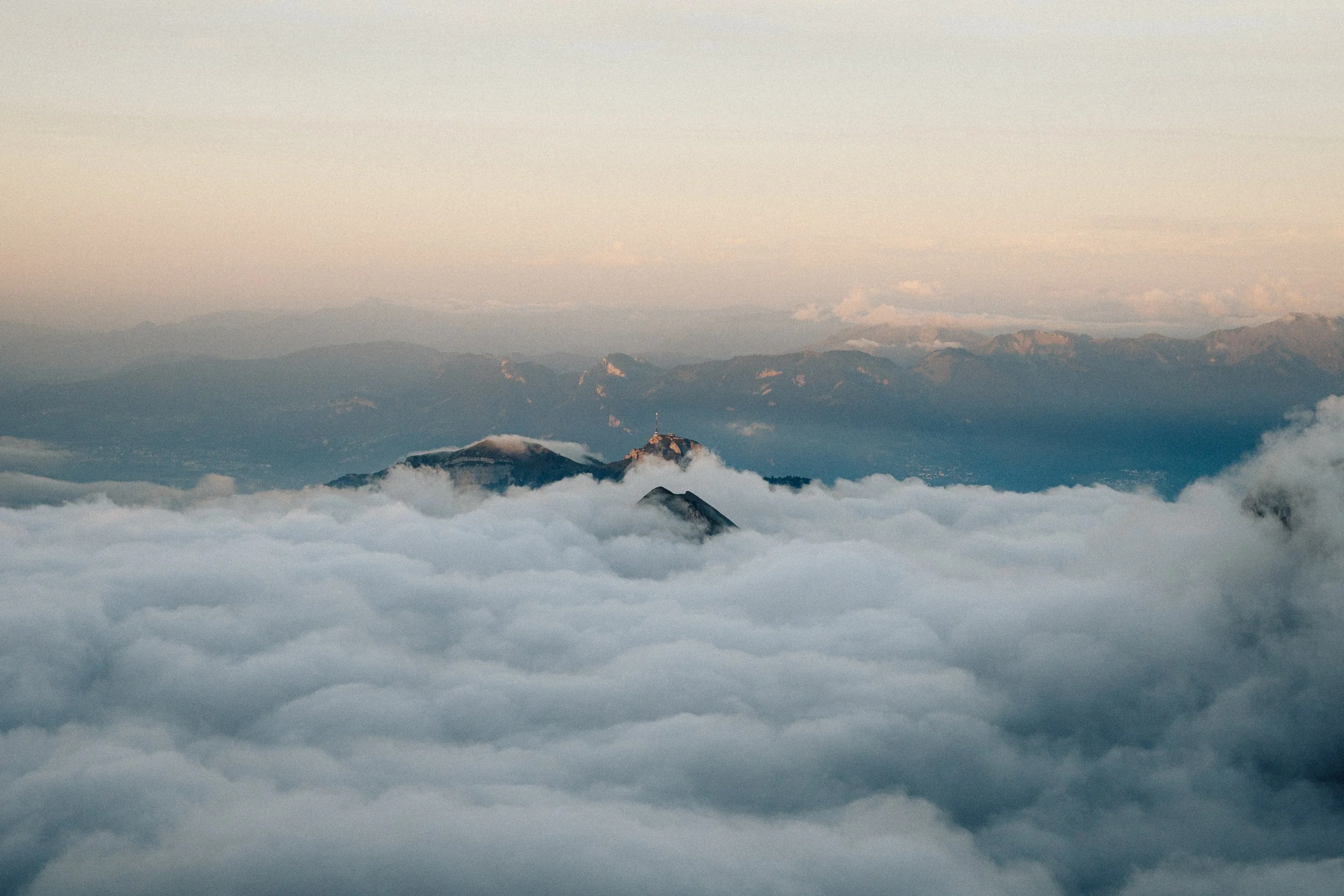 Mountain peaks rising above a thick layer of clouds during sunrise or sunset.