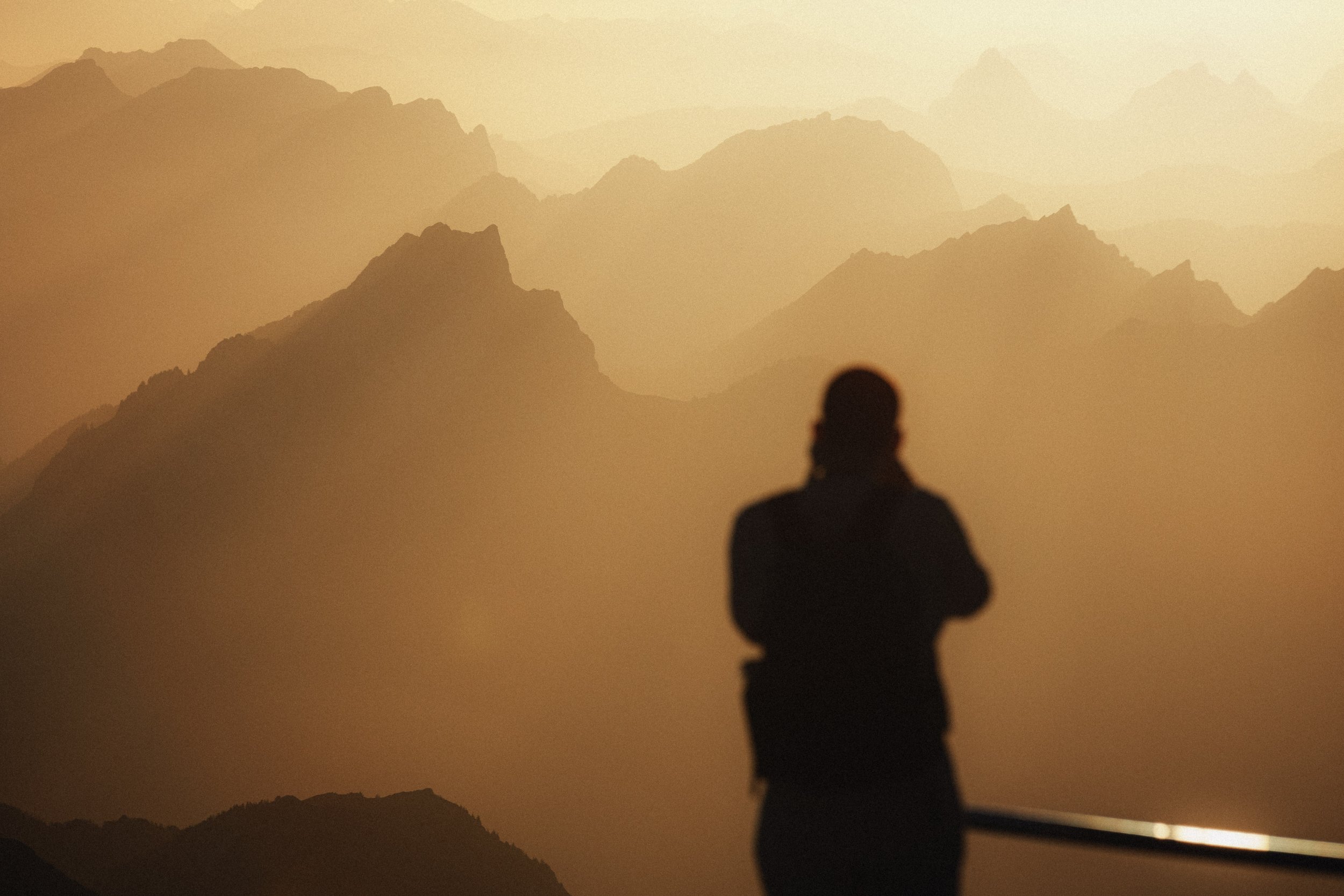 Silhouette of a person standing and looking at a mountain range during sunrise or sunset.