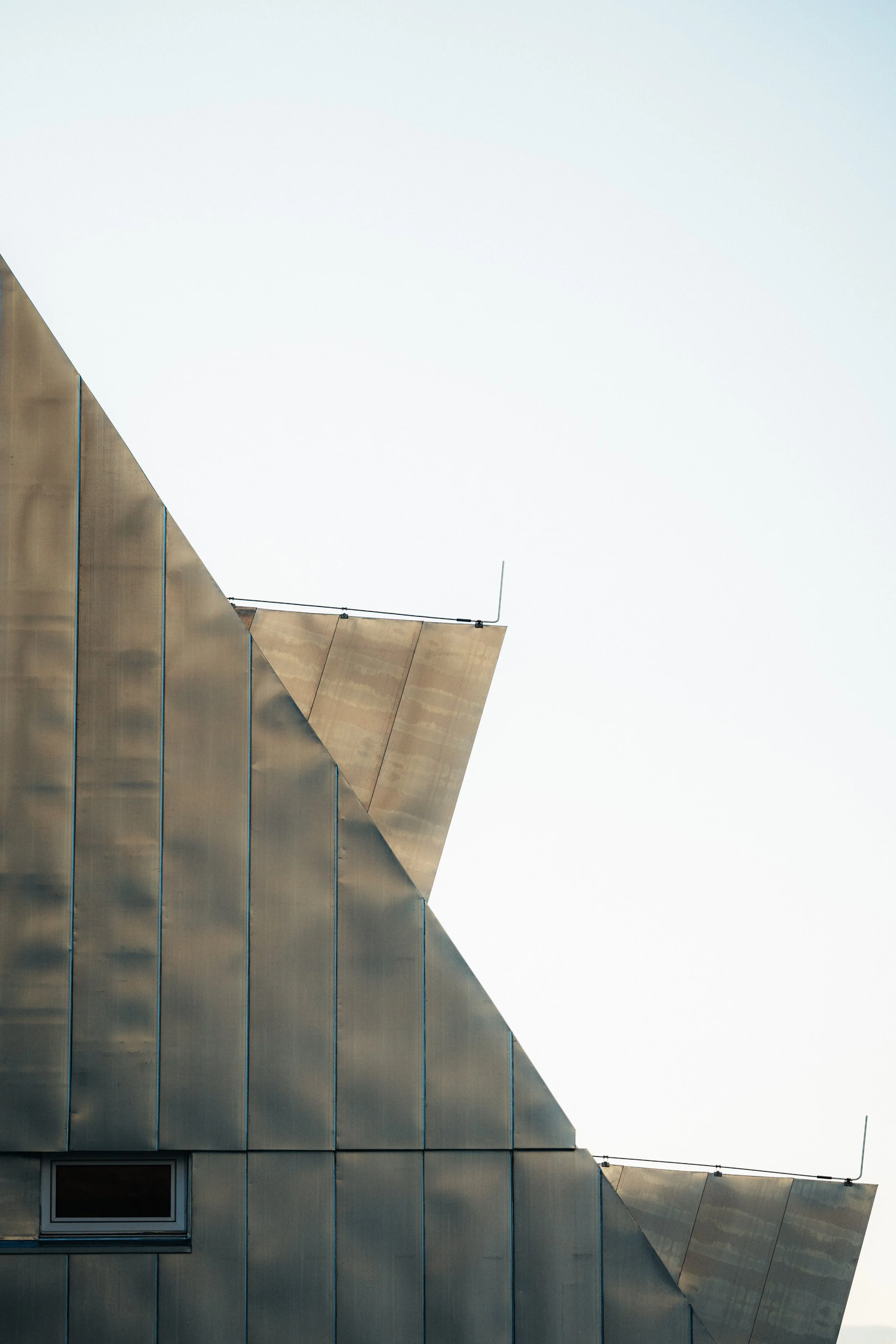Close-up of a modern building with metallic panels and sharp, angular rooflines against a clear sky.