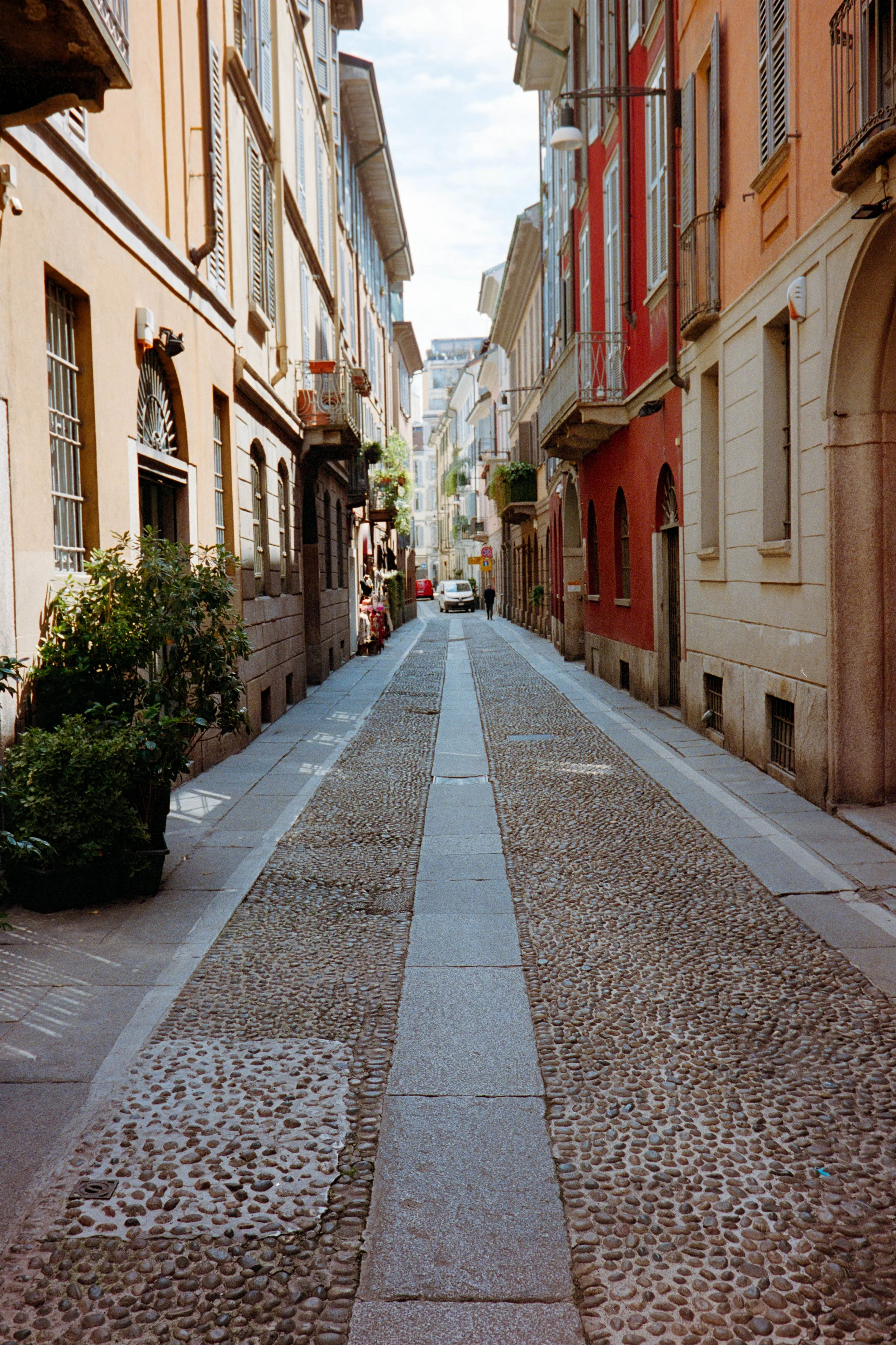 A narrow European street with colorful buildings, cobblestone pavement, and a person walking in the distance.
