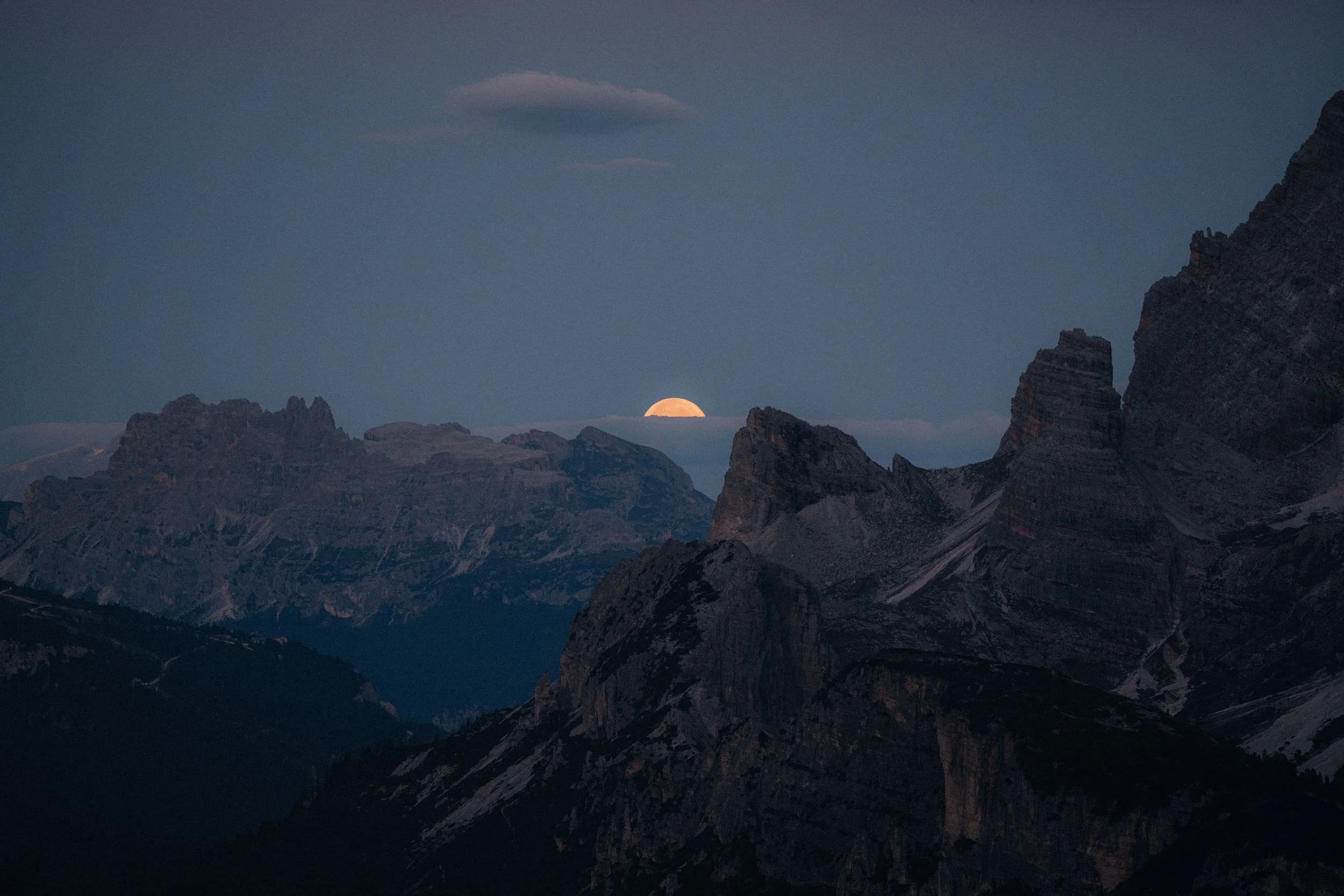 Moon rising over a mountain range during twilight in a remote natural landscape.