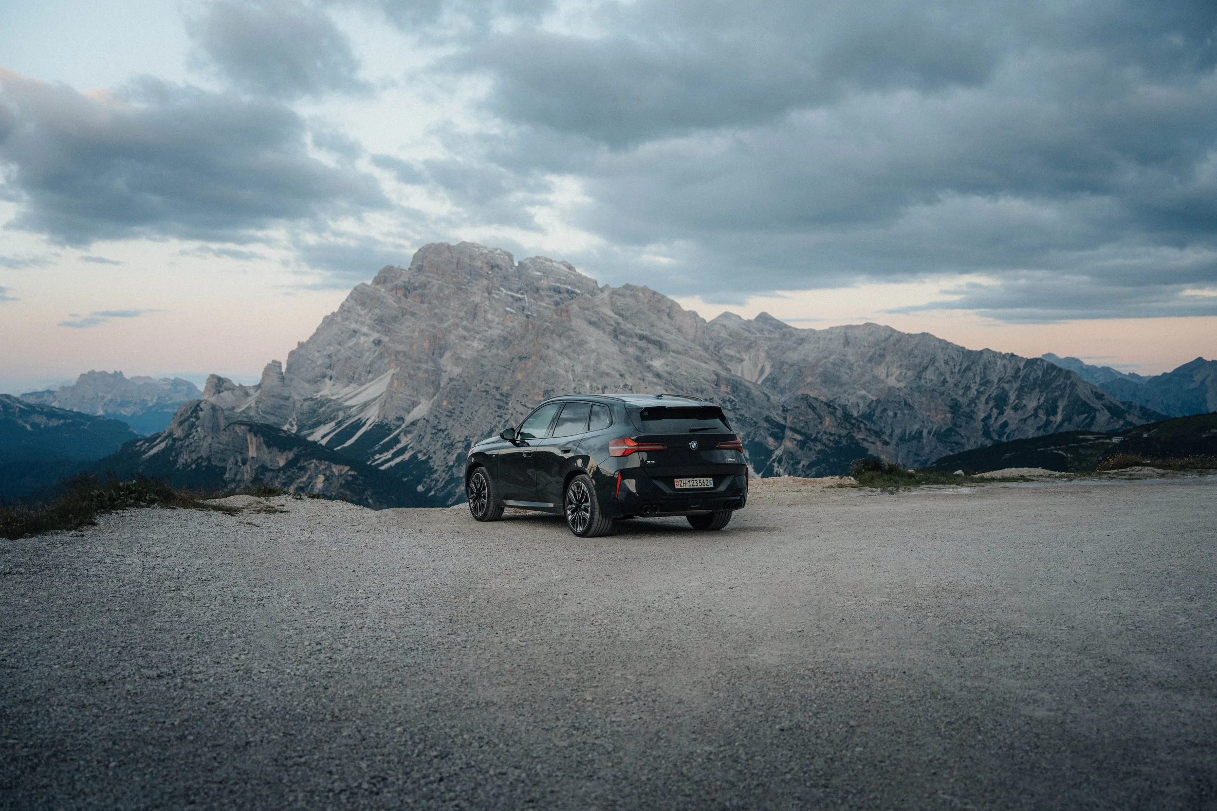 Black SUV parked on gravel road with mountain range in the background under cloudy sky.