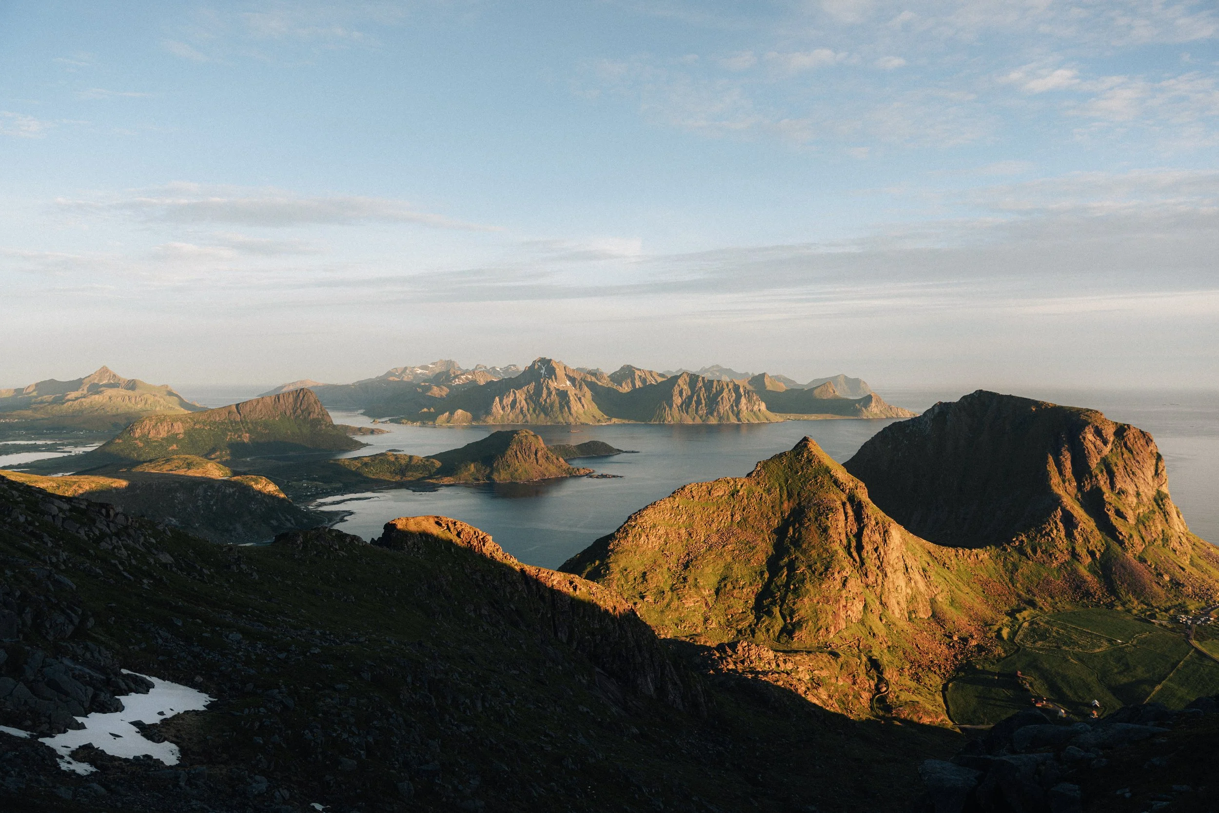Landscape of a mountainous island with green and rocky peaks, a body of water, and distant mountains under a partly cloudy sky