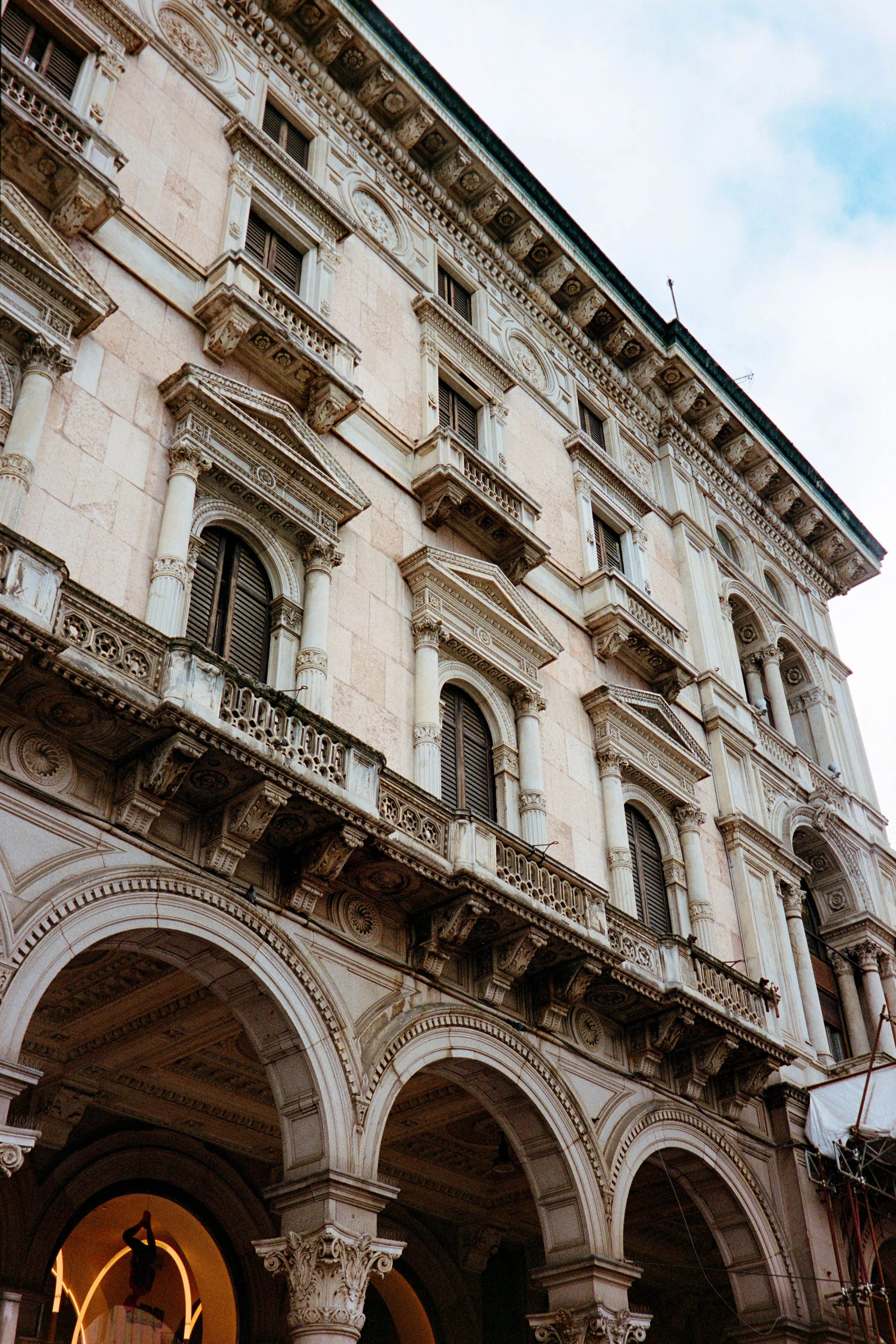 A historic building with ornate architectural details, multiple columns, arched windows, and decorative balconies under a partly cloudy sky.