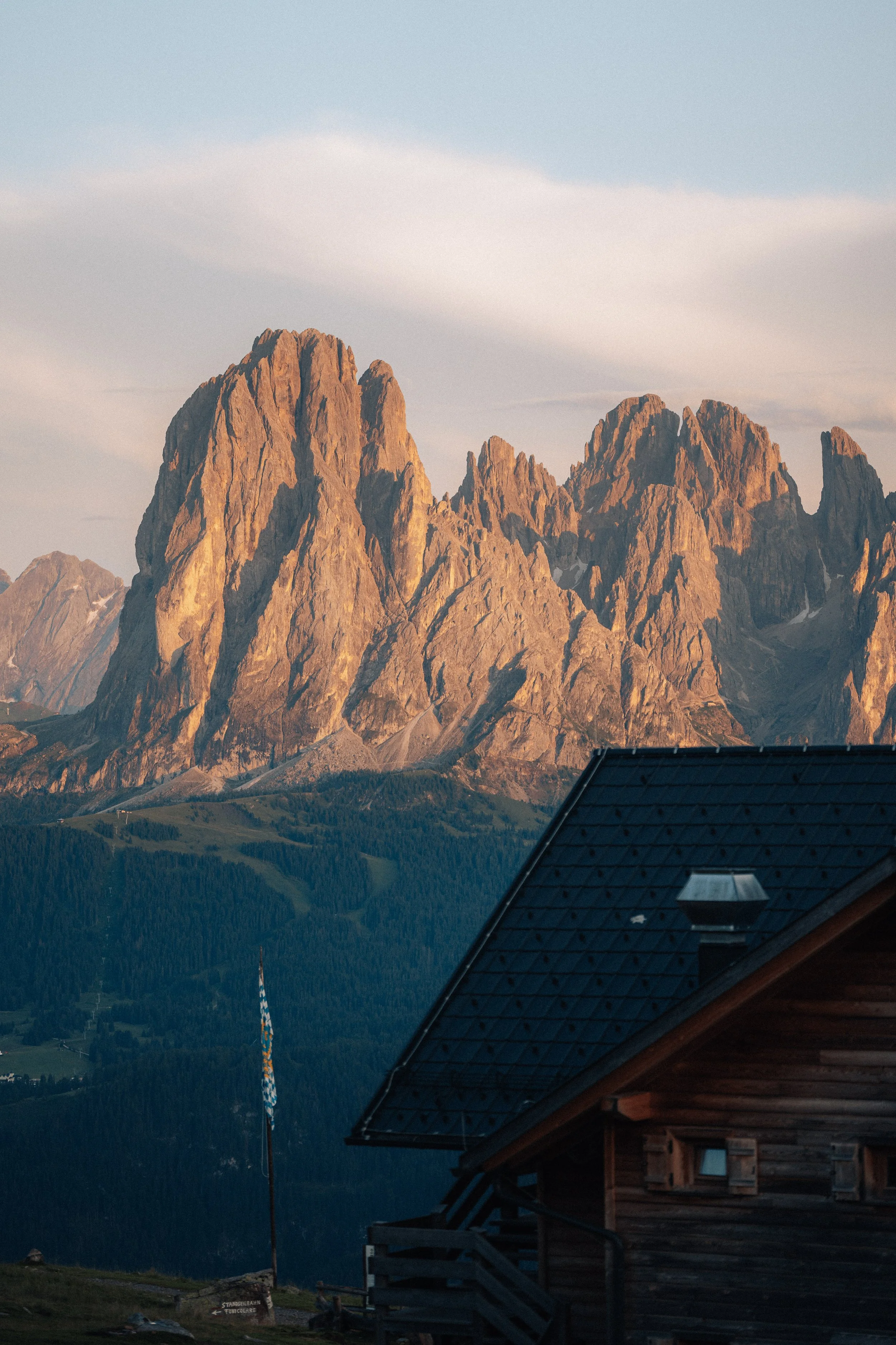 Mountain range at sunset with a wooden cabin and a flag in the foreground.
