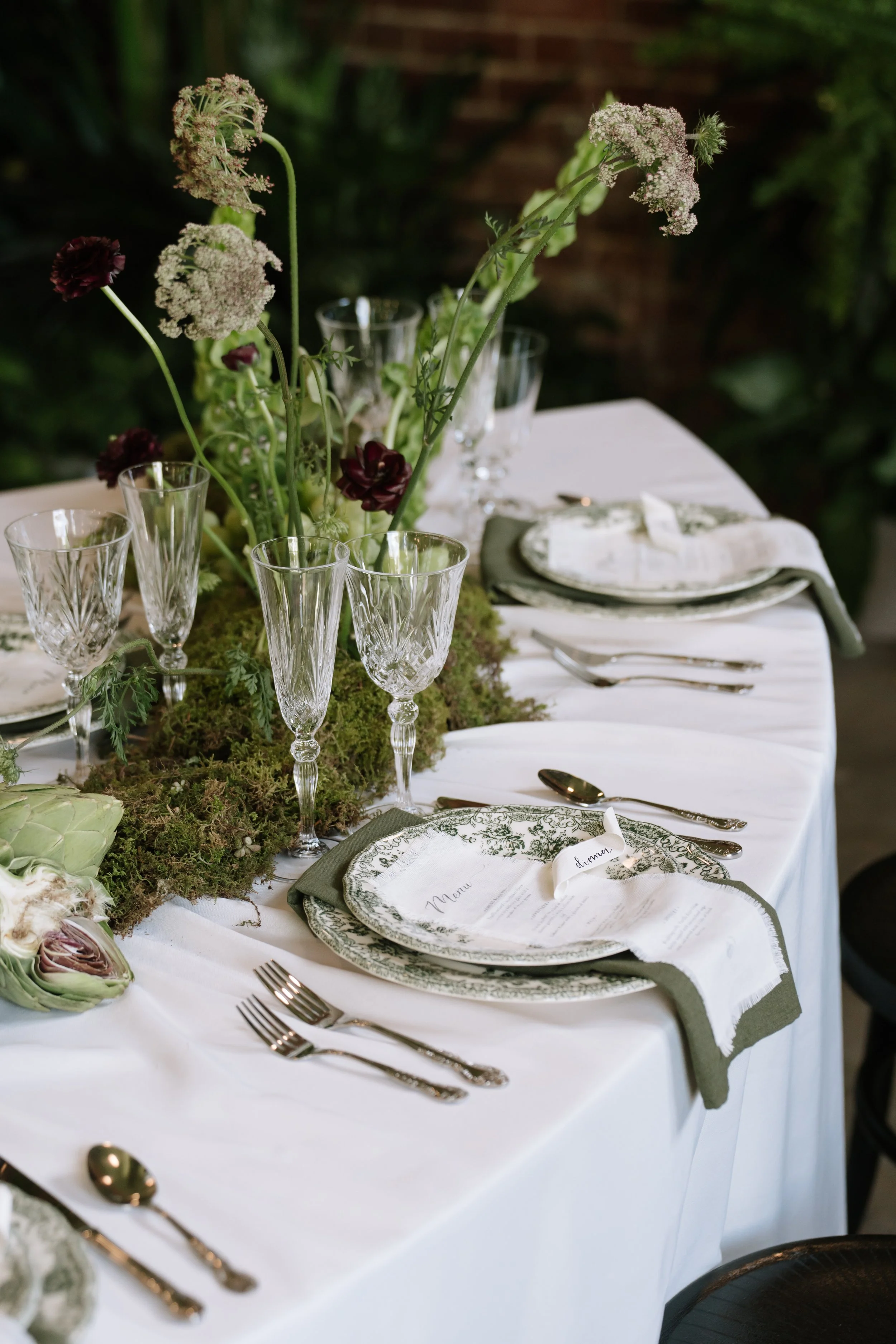 Elegant table setting with crystal glasses, floral centerpiece, and place settings on a white tablecloth, suitable for a formal event or wedding reception.