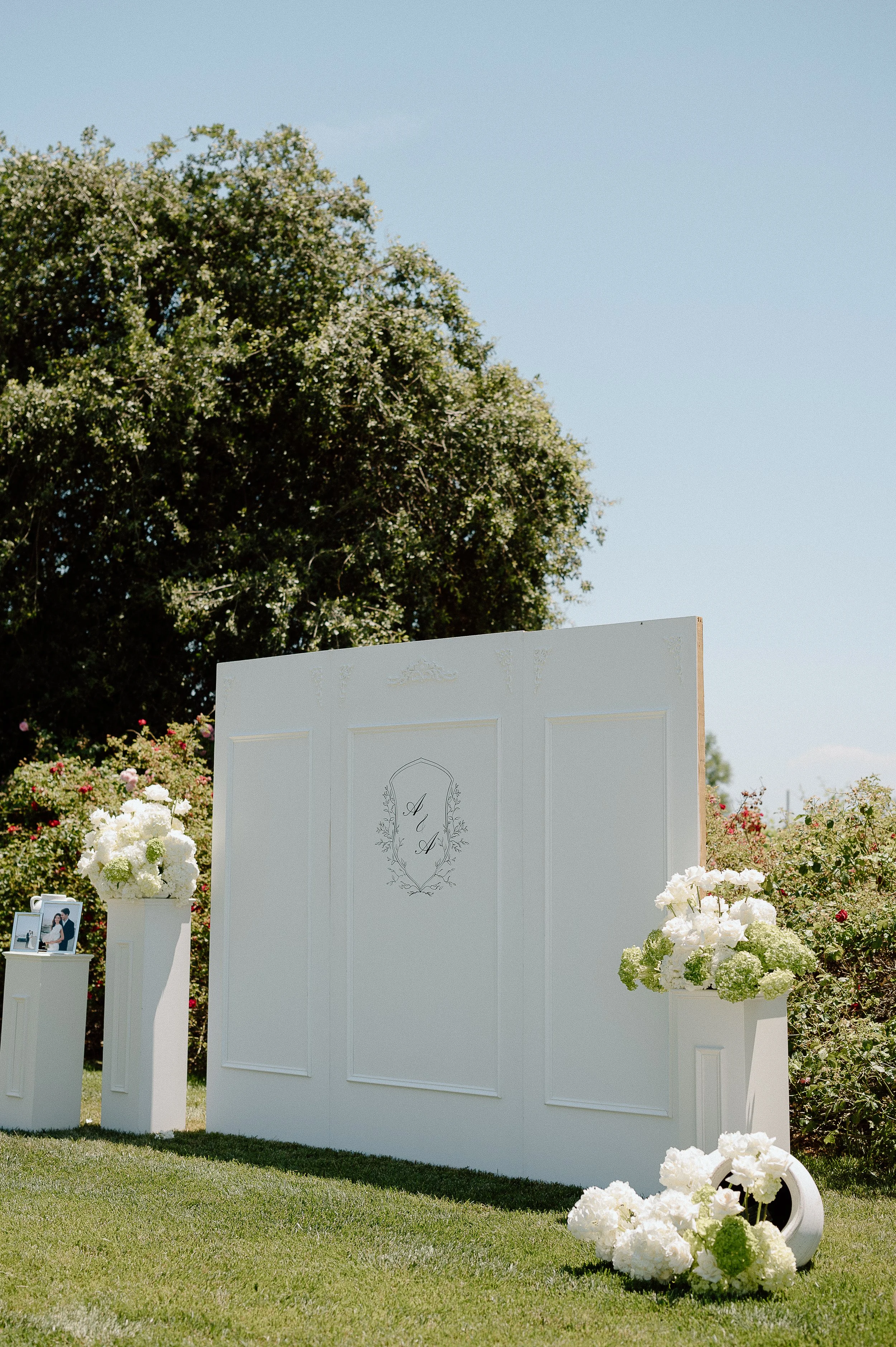 Outdoor wedding setup with floral backdrop showcasing signature tone design, company branding, local embroidery elements, and a quick timeline