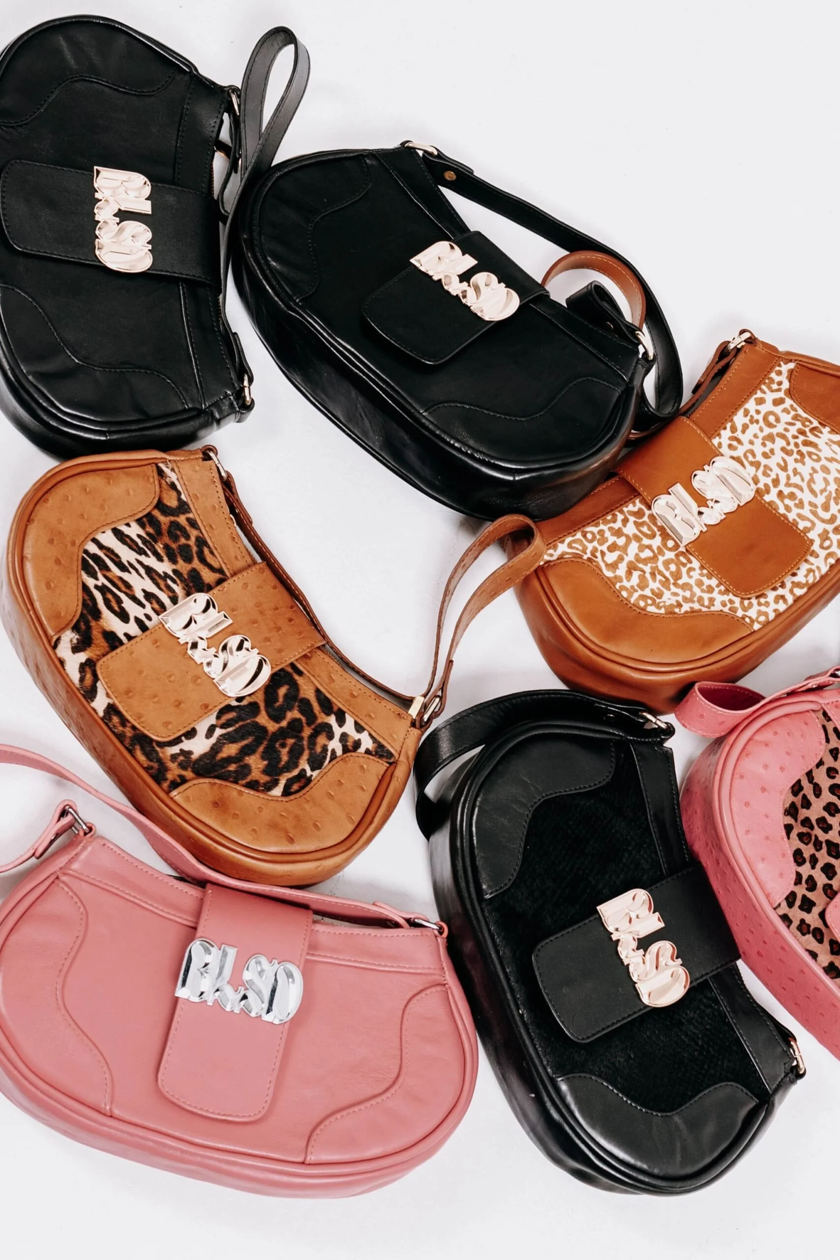 Six handbags with 'BLSO' embellishments arranged on a white surface. The handbags feature a mix of solid colors and animal print designs including black, brown, leopard print, and pink.